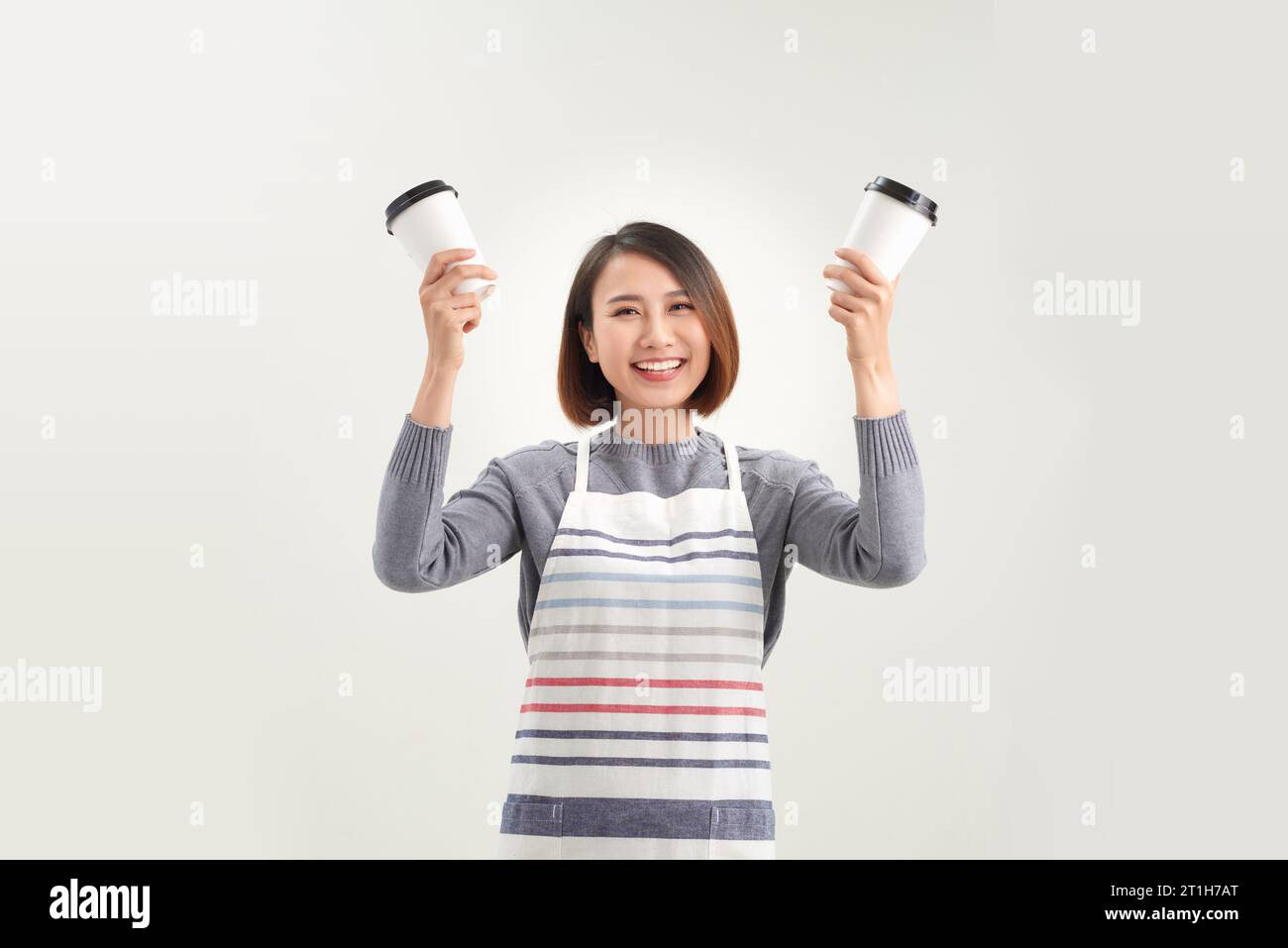 Jeune femme entrepreneur asiatique dans le tablier avec la main tenant tasse de café isolé sur fond blanc Banque D'Images