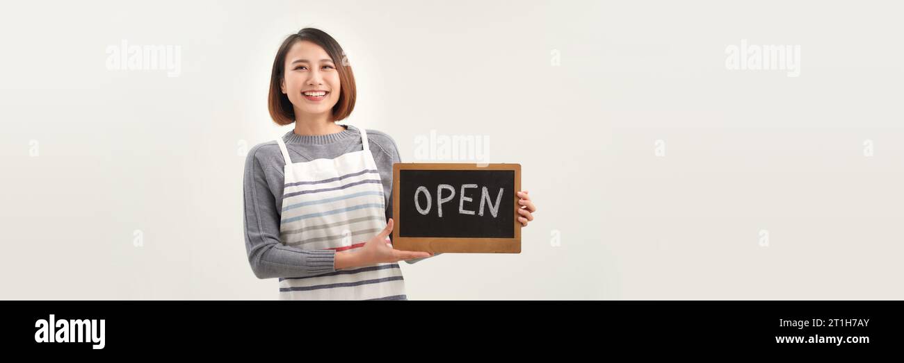 Femme propriétaire d'entreprise dans le tablier tenant le signe OUVERT et souriant isolé sur fond de bannière blanche Banque D'Images