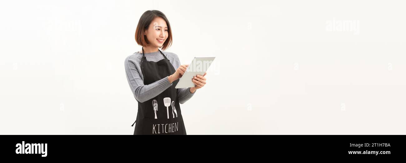 Sympathique mignonne barista féminine en tablier noir souriant à la caméra, en utilisant une tablette numérique pour gérer les commandes de café Banque D'Images