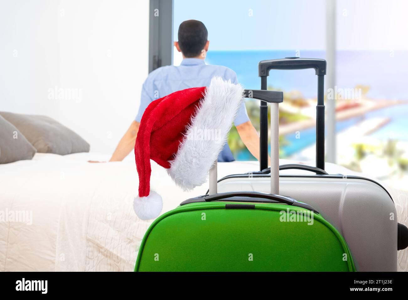 Une valise rouge, un chapeau de Père Noël et un touriste célibataire se relaxant regardant par la fenêtre d'une chambre d'hôtel après être arrivé avec des valises au premier plan Banque D'Images
