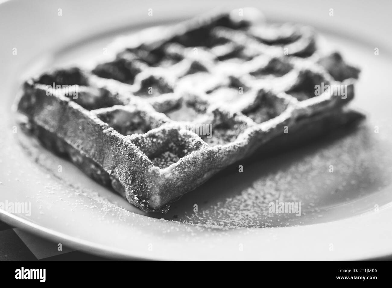 Un portrait en noir et blanc d'une délicieuse gaufre savoureuse belge avec du sucre en poudre comme garniture dessus, couché sur une assiette blanche sur une nappe rouge prête Banque D'Images