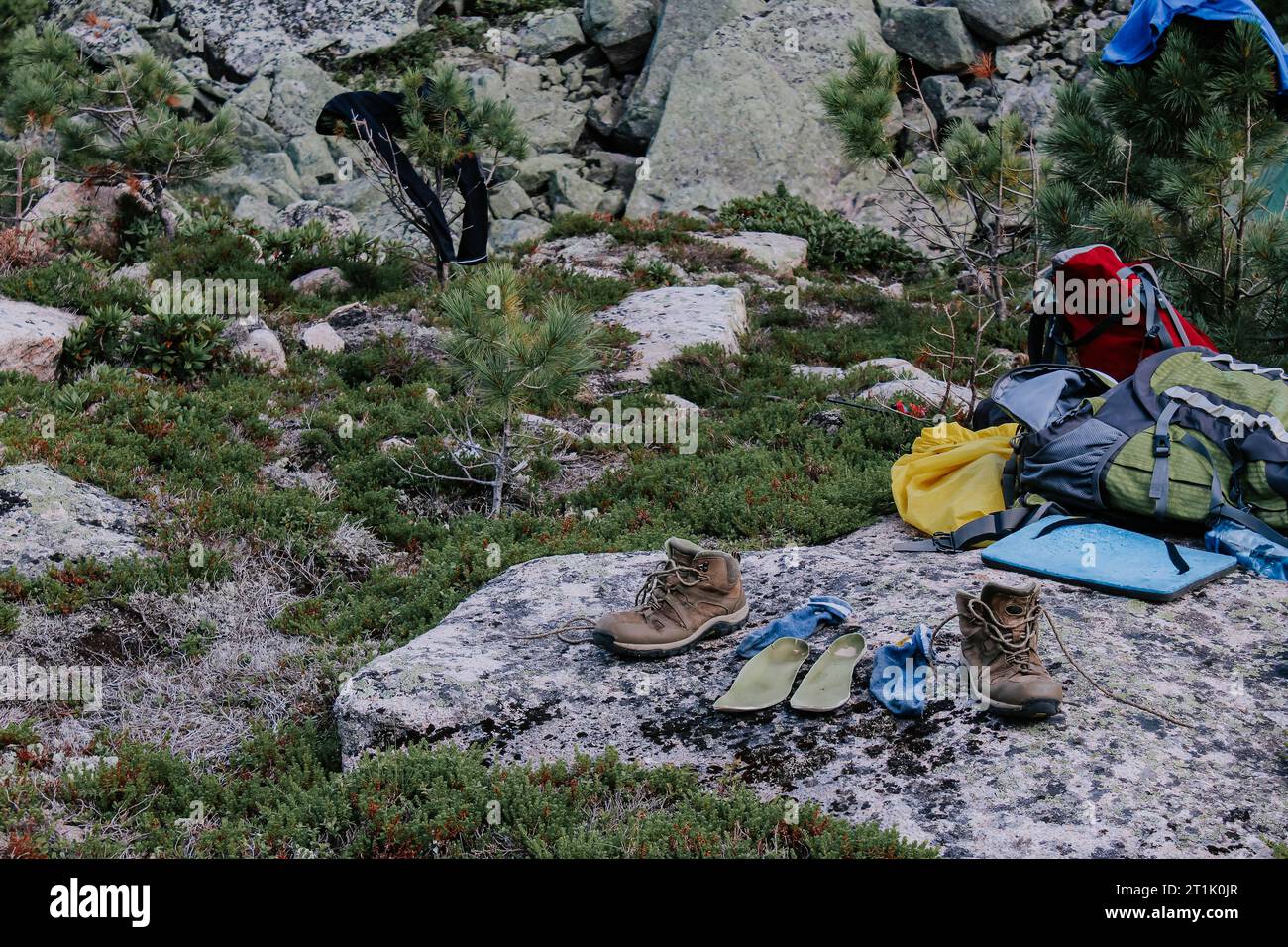 Matériel de séchage après une randonnée au camping. Vieilles bottes de trekking brunes, semelles vertes et chaussettes bleues à sécher après une journée de randonnée, disposées sur pierre. W Banque D'Images