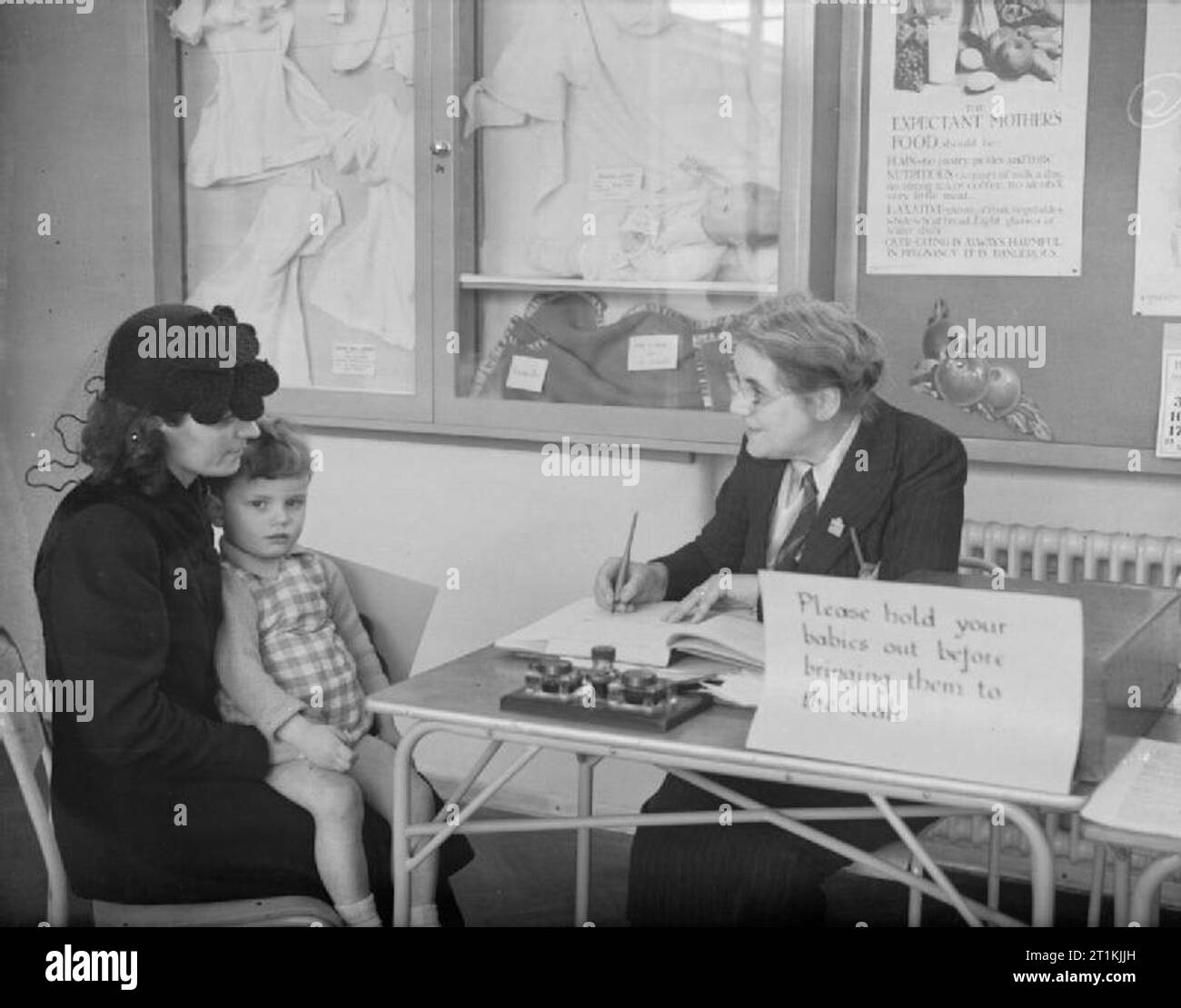 Garderie à Tottenham, Londres, Angleterre, 1940, le superintendant de la garderie municipale Park Lane prend plus de détails d'une mère sur son fils, qui espère commencer à la pépinière à Tottenham, Londres. Notez que le surintendant est le port d'un badge WVS indiquant son implication dans la Women's Voluntary Service. Banque D'Images