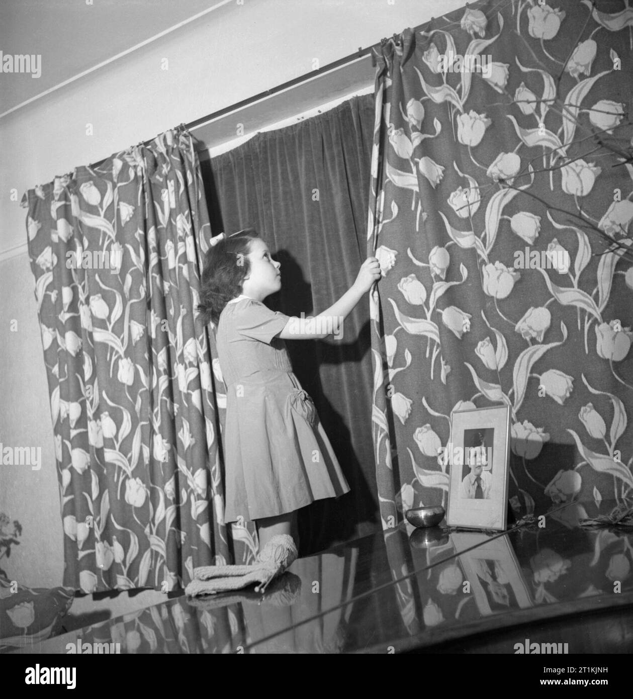 Doreen Buckner tire les rideaux dans sa famille d'accueil Londres pour se conformer à la soirée 'Blackout' pendant la Seconde Guerre mondiale. Sept ans, Doreen Buckner tire les rideaux dans sa famille à Londres, pour la maison. Clairement visible derrière les rideaux à motifs sont les rideaux occultants. Qu'elle se souvienne de la vie peu avant la guerre, en fonction de la légende originale, Doreen ce qui concerne le dessin de la panne "comme une procédure normale dans un monde normal'. Banque D'Images