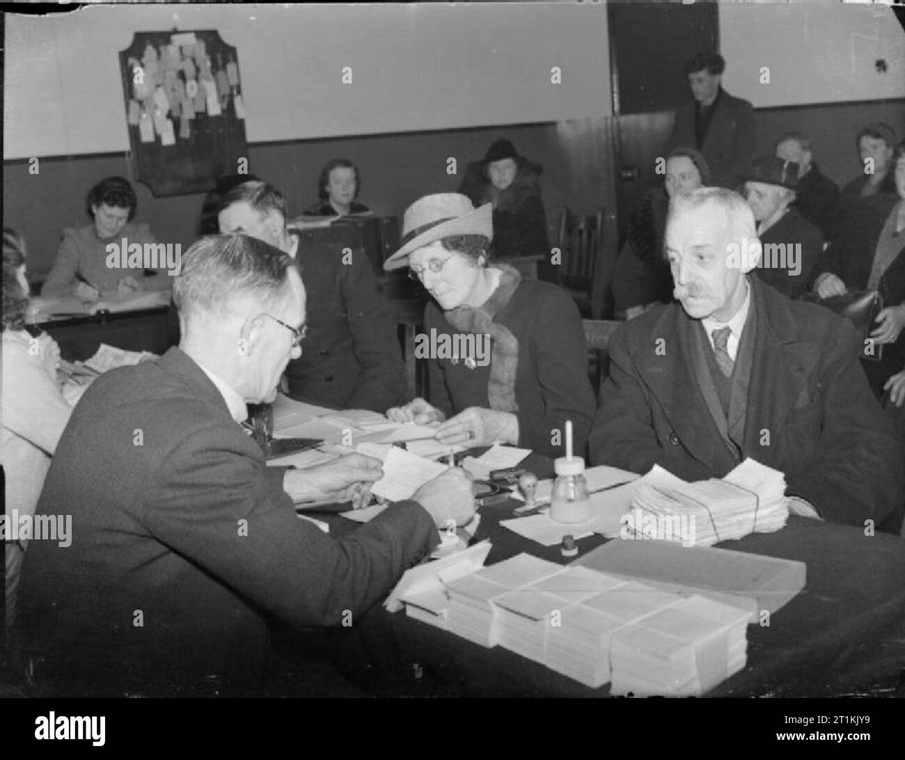 Bureau d'information sur l'aide sociale à l'emploi de la guerre- à Londres, 1941 civils deux personnes âgées parler à un agent d'information dans le relogement et l'hébergement ministère de l'East Ham Information Bureau afin de s'appliquer pour une nouvelle maison après la destruction de leur ancienne maison au cours d'un raid aérien. Dans l'arrière-plan, de nombreuses autres personnes sont assis, attendent patiemment leur tour. Banque D'Images