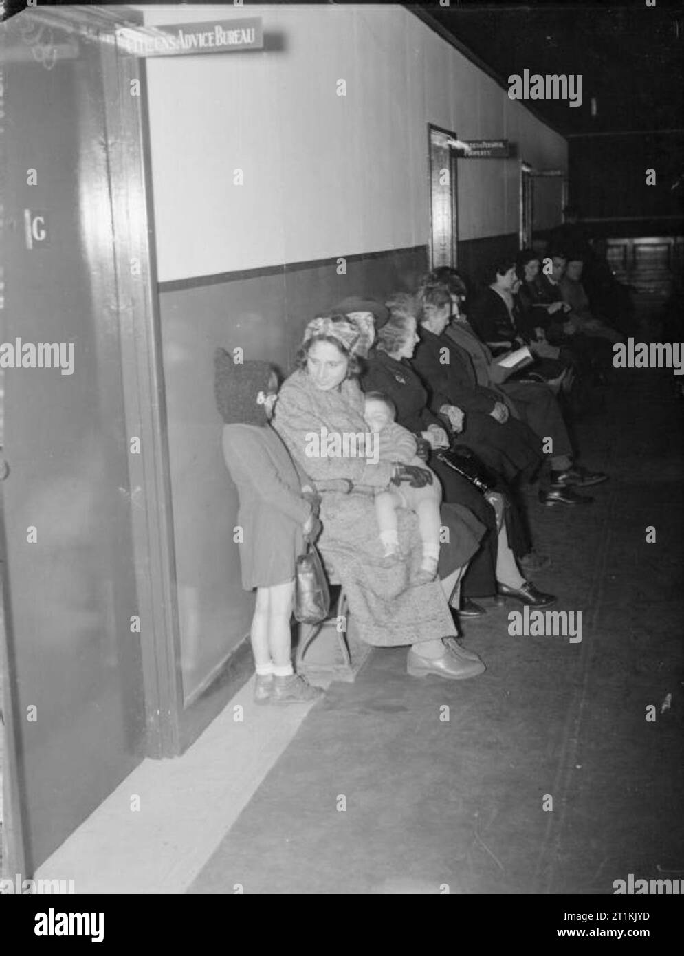 Bureau d'information sur l'aide sociale à l'emploi de la guerre- à Londres, 1941 Hommes, femmes et enfants line le couloir en attendant de trouver de l'aide auprès de certains des ministères basé à East Ham de ville. Au premier plan, ces civils sont en attente de visiter le bureau de conseil aux citoyens et plus loin un signe au-dessus de la porte indique le « blessés et des biens personnels. Une dame qui l'attendaient à ce prix est le tricotage pour passer le temps ! Banque D'Images