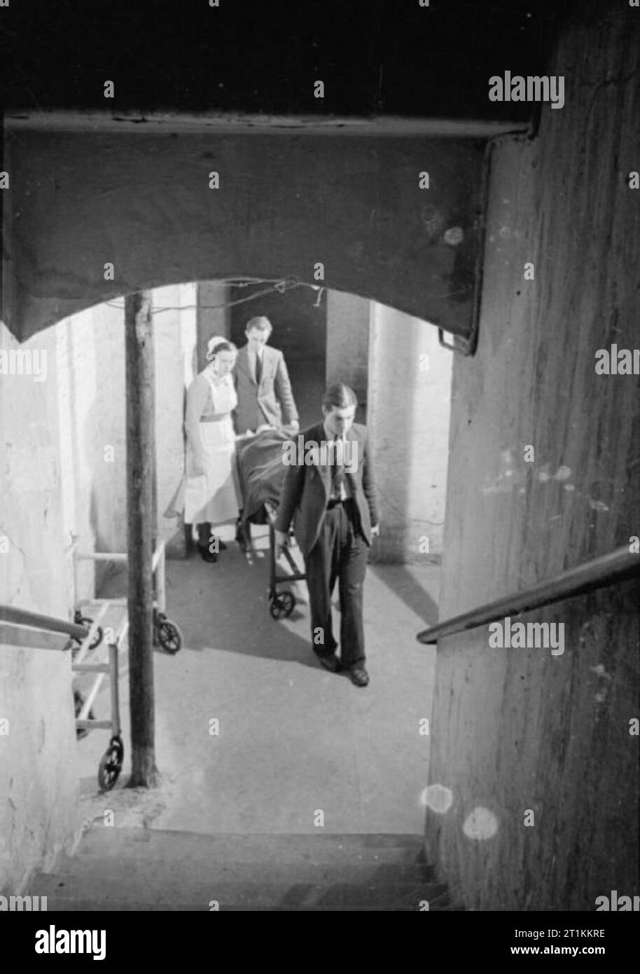 Guy's Hospital- La vie dans un hôpital de Londres, Angleterre, 1941 Une infirmière accompagne deux porteurs comme ils le transport d'un patient dans la salle d'opération dans le sous-sol de Guy's Hospital à travers les souterrains de l'escalier qui mène jusqu'à la tutelle. Le patient semble être allongé sur un chariot de l'hôpital. Banque D'Images