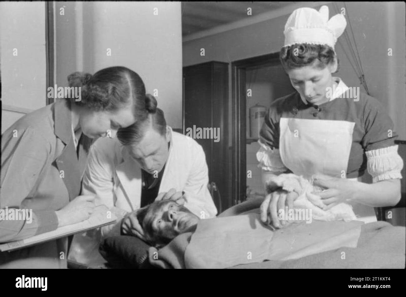Guy's Hospital- La vie dans un hôpital de Londres, Angleterre, 1941 Un médecin et l'infirmier au London's Guy's Hospital s'occuper d'un patient dans la chirurgie de l'hôpital, alors qu'un aumônier (sur la gauche de la photographie) prend les détails personnels de la victime et de ses mises à jour de MPC 47 forme, qui contient toutes les informations sur le patient à partir de leur entrée à l'hôpital et sera utilisé pour disposer d'autres soins ou de traitement. Banque D'Images