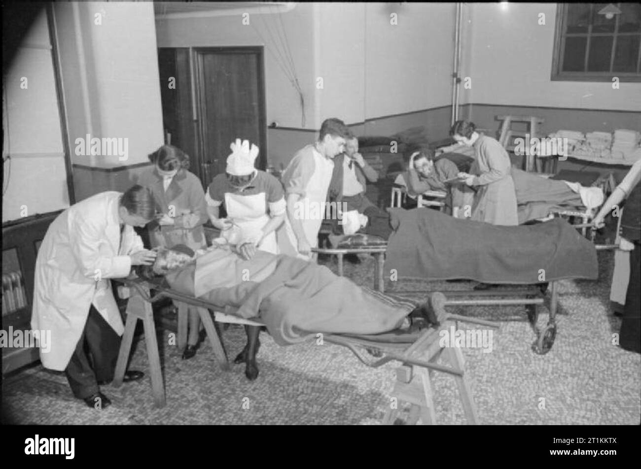 Guy's Hospital- La vie dans un hôpital de Londres, Angleterre, 1941, des brancards sont transportés jusqu'à la chirurgie à Guy's Hospital, où les médecins, infirmières et patients pour assister à almoners. Deux patients sont sur trollies, mais l'un dans l'avant-plan est toujours couché sur le brancard en acier sur lequel ils ont été amenés à l'hôpital. La civière a été équilibré sur deux cadres en bois UN pour permettre aux membres du personnel de l'hôpital pour assister au patient. L'almoners prise de coordonnées des patients pour leur permettre de prendre des dispositions pour l'après-soin. Banque D'Images