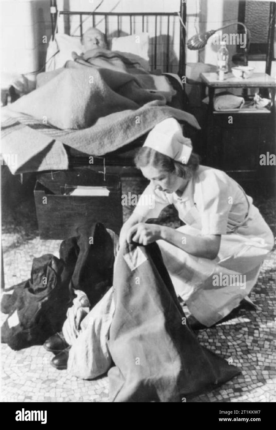 Guy's Hospital- La vie dans un hôpital de Londres, Angleterre, 1941 Une infirmière recueille l'ensemble des vêtements et effets personnels d'un patient, qu'il dort dans le lit derrière elle sur un ward au Guy's Hospital de Londres en 1941. Tous les vêtements retirés de blessés sont placés dans des sacs verts avec le nom de la victime sur eux. Banque D'Images