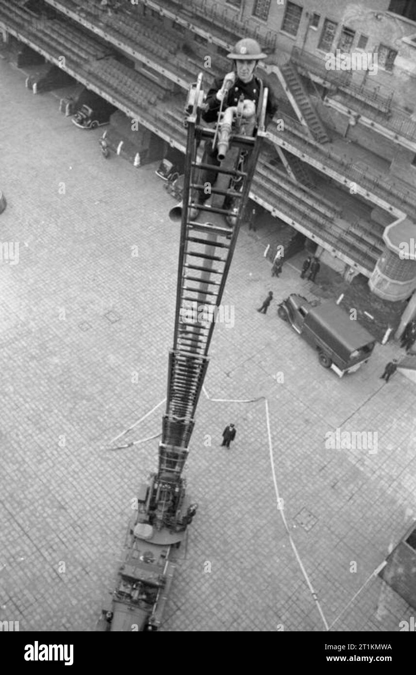 Londres- Afs hommes du feu auxiliaire Service à Londres, C 1940 membre de l'Auxiliaire de Service des incendies se trouve au sommet d'une échelle étendue-en partie lors d'un exercice d'entraînement à la London Fire Brigade. Banque D'Images