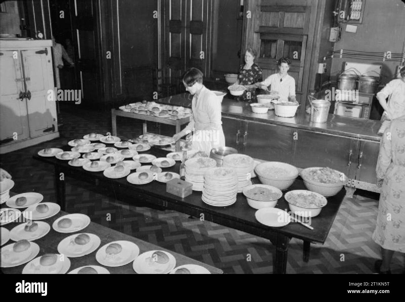 Les Londoniens' Service Repas- à la cantine de poissonnerie Hall, London Bridge, Londres, 1942, un cuisinier prépare des rouleaux de plaques, la margarine et le fromage dans la cuisine des Londoniens' Service repas à la cantine de poissonnerie Hall, tandis que deux de ses collègues du personnel de cuisine préparer les légumes derrière elle. Banque D'Images