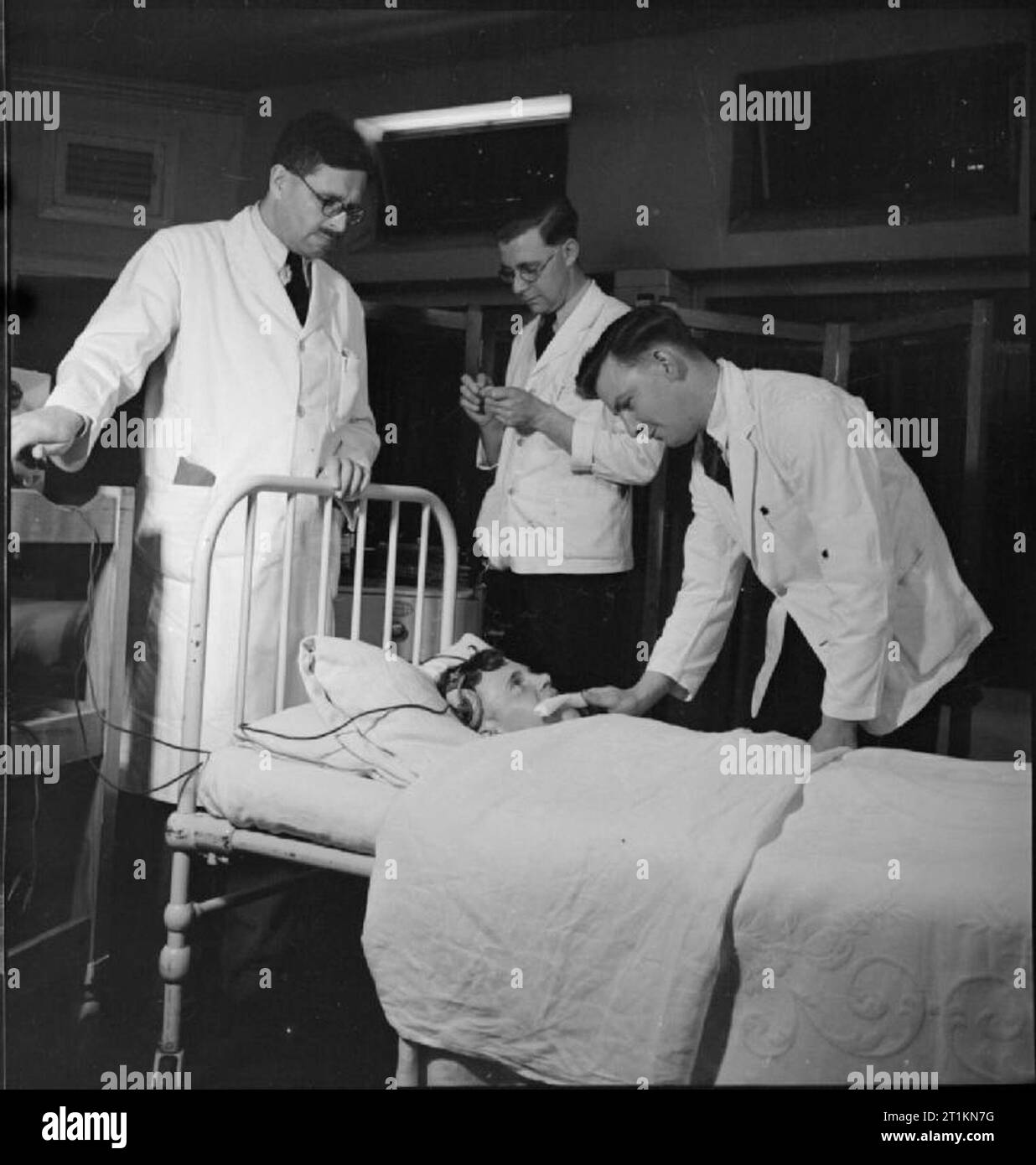 Les hommes en soins infirmiers- La vie à l'Hôpital d'Runwell, Wickford, Essex, 1943 Un infirmier à l'Hôpital d'Runwell insère un bâillon dans la bouche d'un patient que le médecin (à gauche) se prépare à commencer un traitement antiépileptique. Un second mâle infirmière prépare les électrodes. Banque D'Images