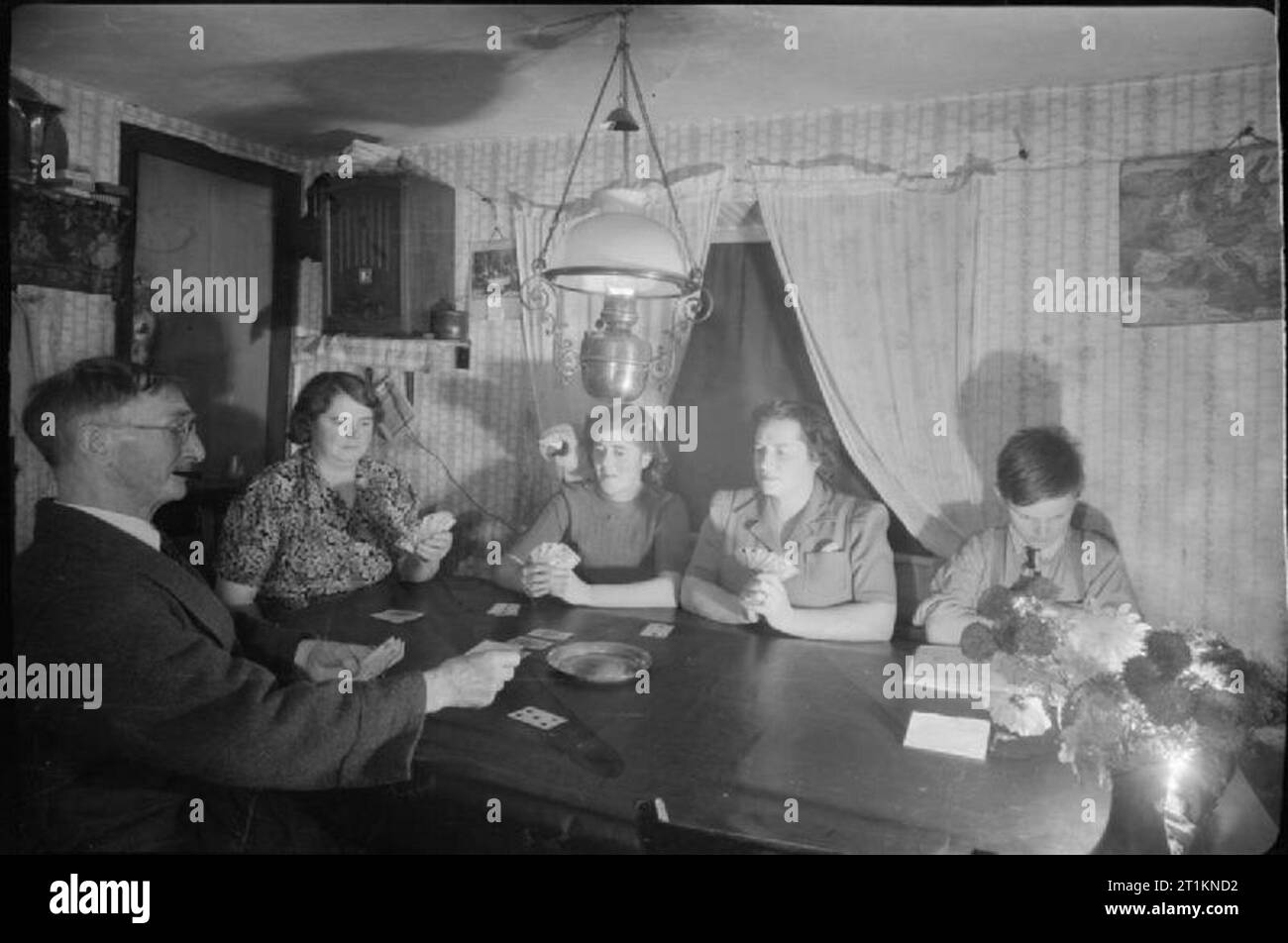 L'épouse de sergent au Moyen-Orient du signaleur ne travail- la vie comme un chemin de fer Signalwoman, Molland, Devon, Angleterre, RU, 1943 Signalwoman Daisy Cook, deuxième à partir de la droite, bénéficie d'un jeu de Newmarket à Furze Hill Farm, Molland, Devon. Cartes à jouer avec elle sont l'agriculteur Bill Petts, sa gouvernante Mme Ayre et Mme Ayre's daughter Phyllis. La lecture d'un livre sur le droit de la photographie est Bill Petts' 12 ans, petit-fils, Frank. Assis sur l'épaule de Phyllis est macaw, qui était un présent de M. Petts' fille, qui est une infirmière en Inde. Daisy est un séjour à Furze Hill Farm pour la durée de la guerre, ayant Banque D'Images