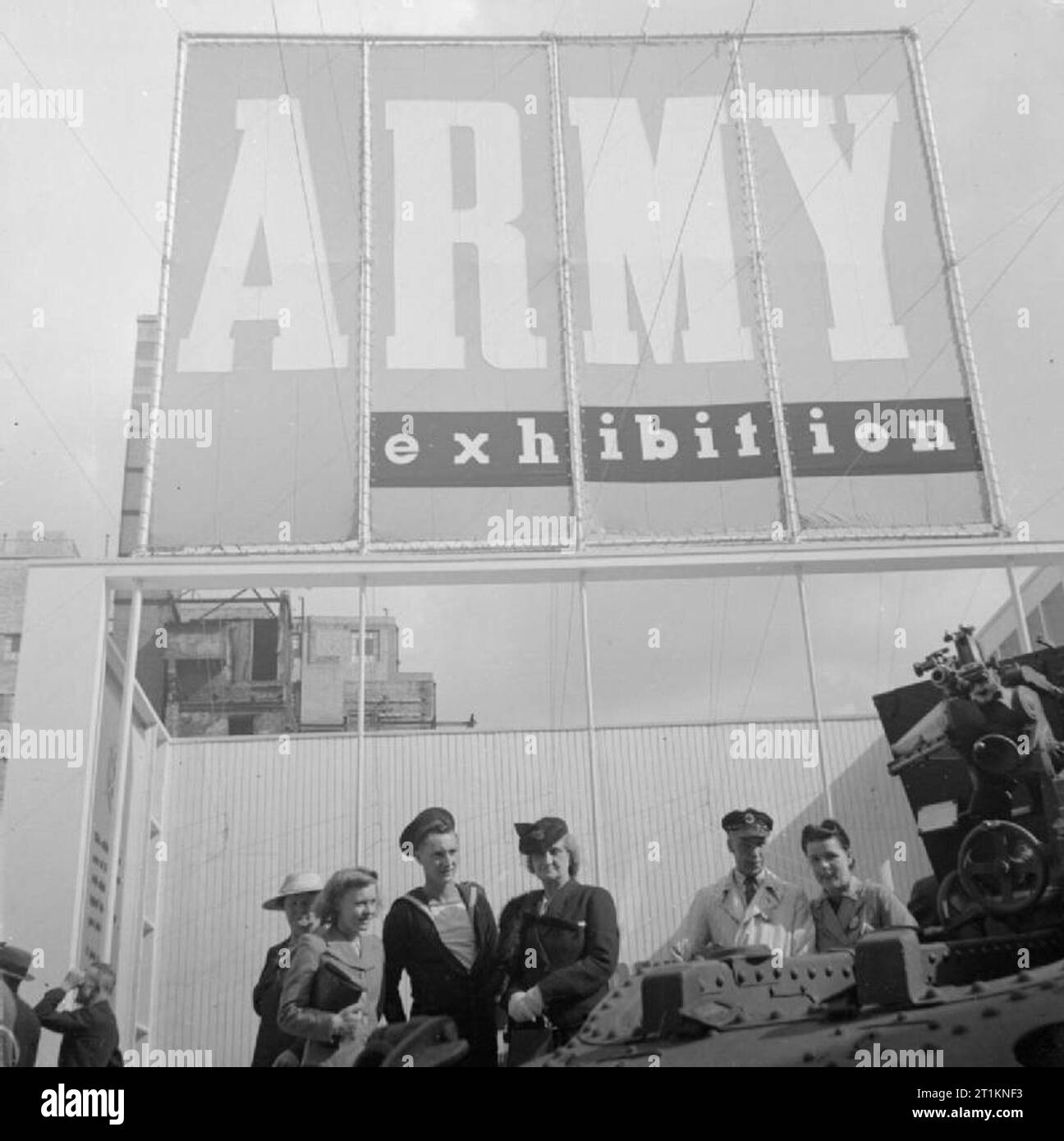 Ministère de l'information expositions pendant la Seconde Guerre mondiale, Londres, Angleterre, RU, 1943 UN MARIN, les travailleurs du secteur des transports et plusieurs civils examiner d'une exposition à la grande exposition de l'armée sur le site bombardé de la John Lewis magasin sur Oxford Street de Londres. La photographie est dominé par la grande bannière annonçant l'exposition, qui peut être clairement vu au-dessus de leurs têtes. Banque D'Images