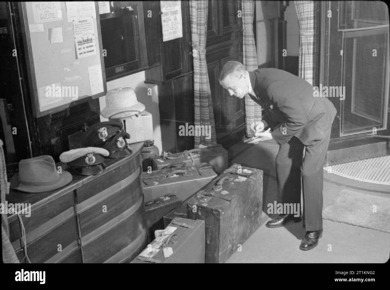 Hôtel de la Marine La Marine marchande- hébergement à Bedford Square, Londres, Angleterre, RU, 1944 M. R W Smith, chef Portier à l'Hôtel de la marine marchande sur Bedford Square, les contrôles sur les bagages des clients nouvellement arrivés dans le hall de l'hôtel. Le tableau d'affichage au-dessus de sa tête pour que les informations pour les clients et il y a aussi des listes de "What's on" à Londres. Selon la légende originale, M. Smith est un vieux marin, qui le premier prend la mer en 1902. Banque D'Images