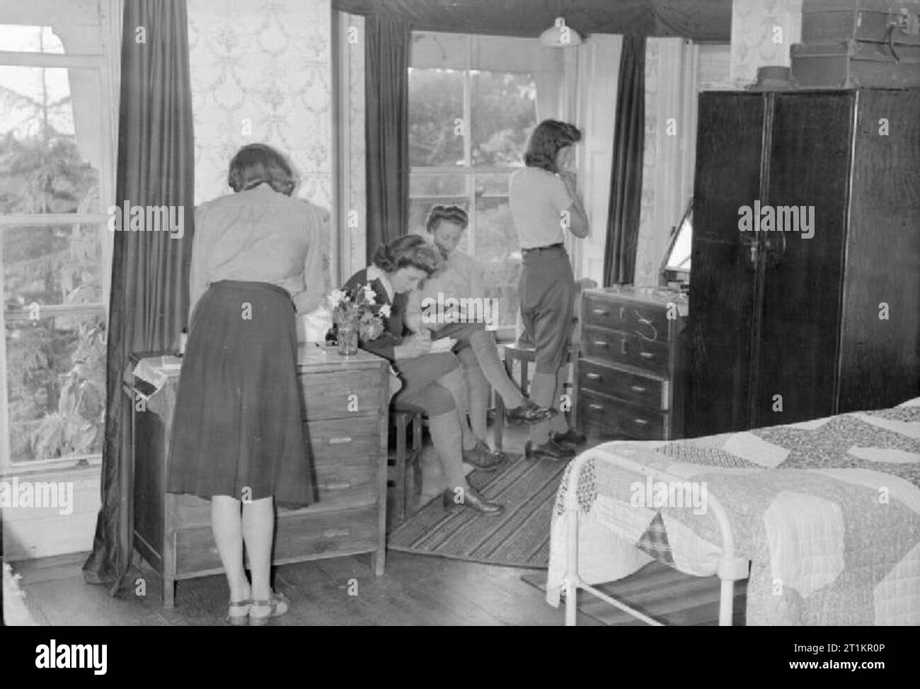 Maison de repos pour Women's Land Army- Repos et détente à Torquay, Devon, Angleterre, RU, 1944 quatre filles se détendre dans la chambre qu'ils partagent à l'automatisation de la maison de repos à Torquay. Deux sont d'écrire des lettres et une autre est de vérifier son apparence dans le miroir. Le prix semble être confortablement meublées. Banque D'Images