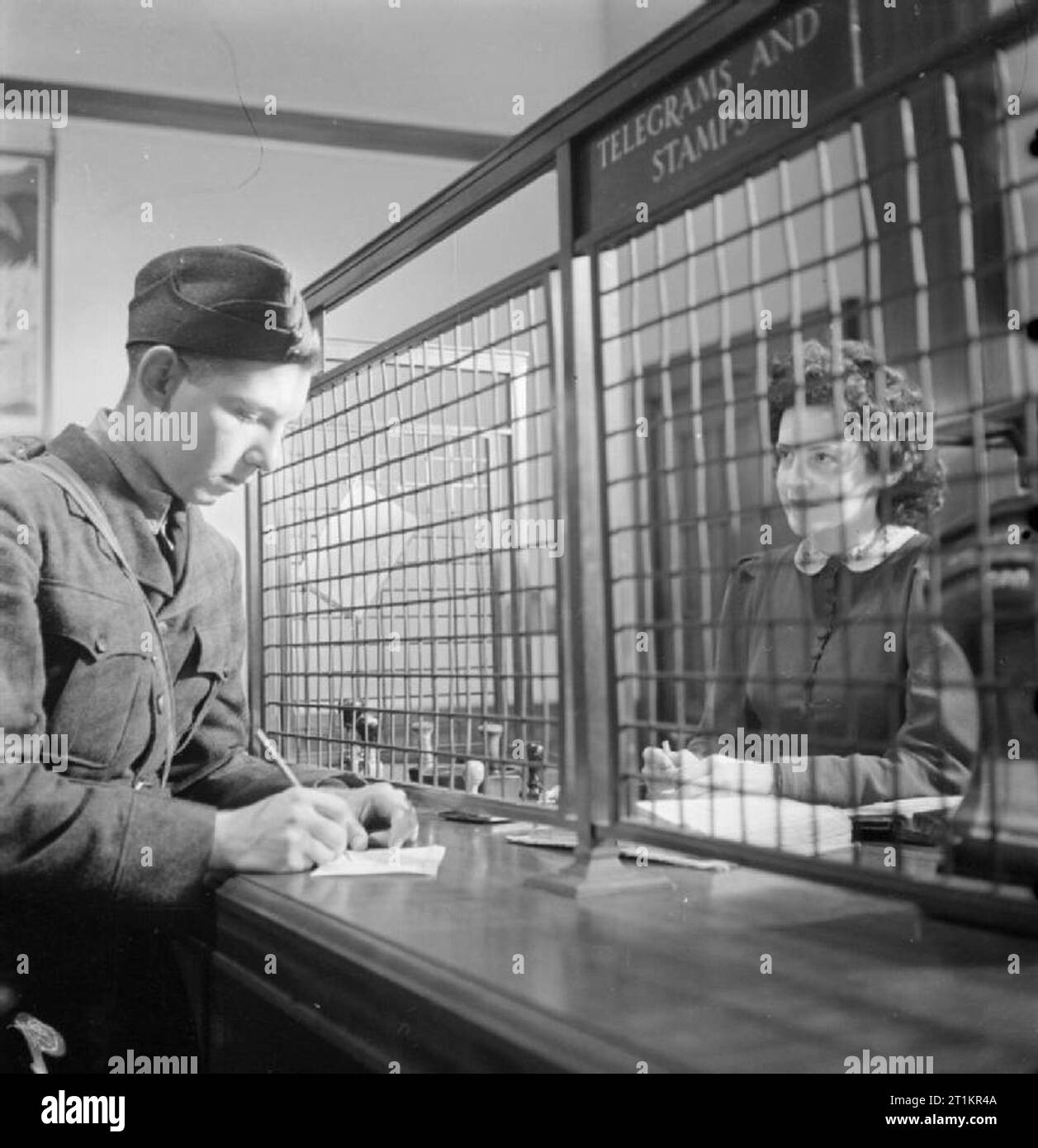 American Boy Meets Girl britannique- Amour et romance sur le front intérieur, Bournemouth, Angleterre, 1941 Robert 'Bob' Ames écrit une famille d'accueil par câble aux États-Unis d'Amérique à la poste, à Bournemouth, en tant que 'MNorah' Mickey McMullen regarde de derrière la grille. Banque D'Images