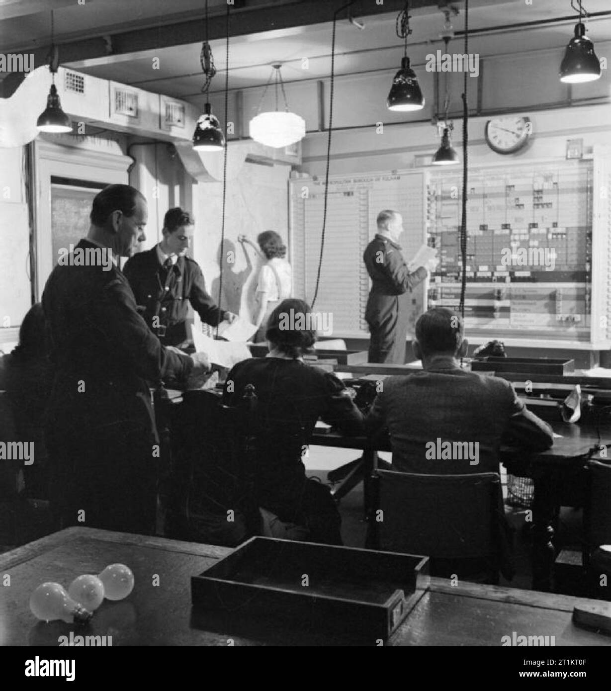 La reconstruction de 'l'Incident'- Formation en protection civile à Fulham, London, 1942 une longue scène dans la salle de contrôle de l'incident. Dans l'arrière-plan une jeune femme le tracé de l'incident sur une carte, tandis que le Greffier à l'agent responsable est la suppression des onglets de l'Panneau de contrôle et de les placer sur l'Incident de bord. Au premier plan, la main des messagers à formes représentants des chefs des divers services de secours. Banque D'Images