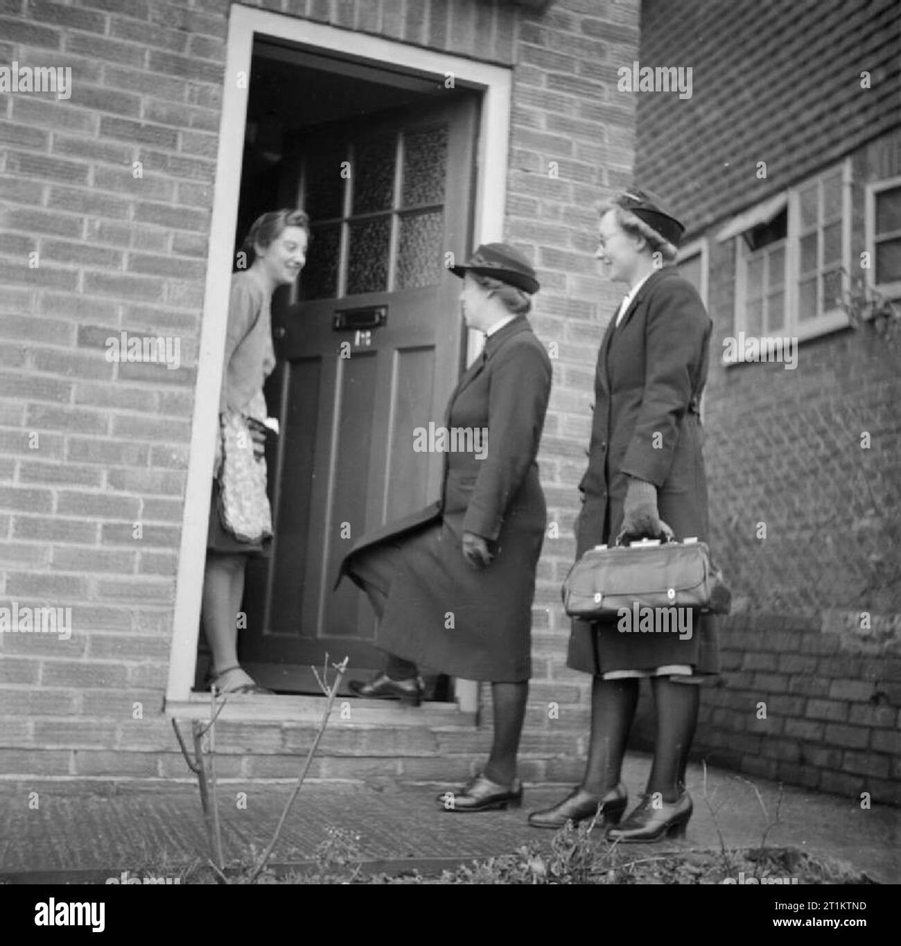 La formation des infirmiers et infirmières de district Queen- La formation des infirmières au Queen's Institute de soins infirmiers de district, Guildford, Surrey, Angleterre, RU, 1944, une stagiaire infirmière de district (droite) accompagne une infirmière de district qualifié lors d'une visite à domicile. Ils sont accueillis à la porte par une femme au foyer. Il est probable que c'est la mère de la jeune fille se remettent d'une pneumonie, comme vu dans D 23115. Banque D'Images