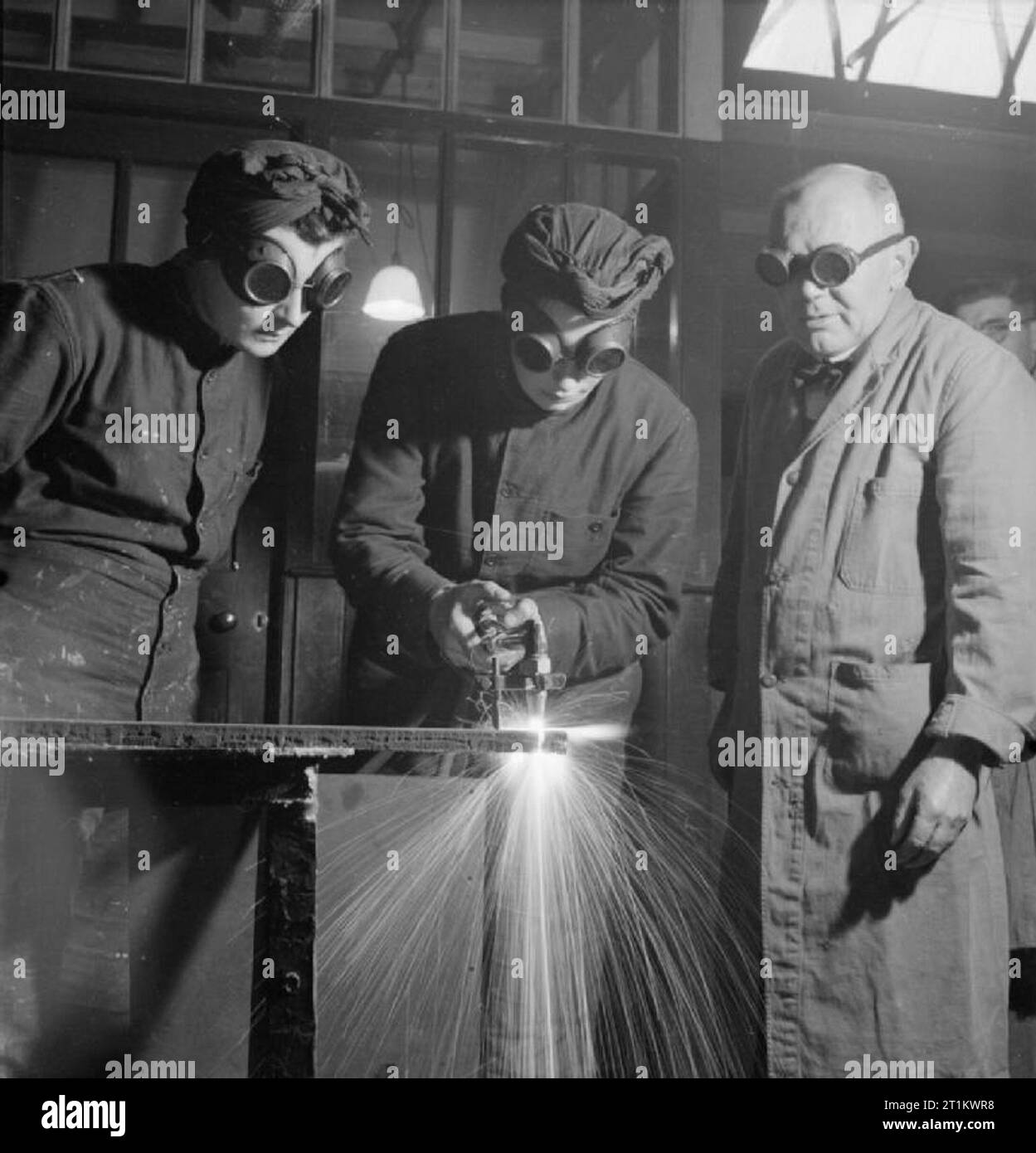 Les roitelets Train pour nouvel emploi- formation pour expédier mécanique de la Women's Royal Naval Service, Angleterre, RU, 1943 étincelles voler en tant que membre de l'WRNS coupe une barre de fer à l'aide d'un chalumeau oxyacéthylénique dans le cadre de sa formation pour devenir un mécanicien de navire (LC), probablement au centre de formation du Gouvernement de Slough. Elle est surveillée par son instructeur et un autre Wren. Tous portent des lunettes de protection. Banque D'Images