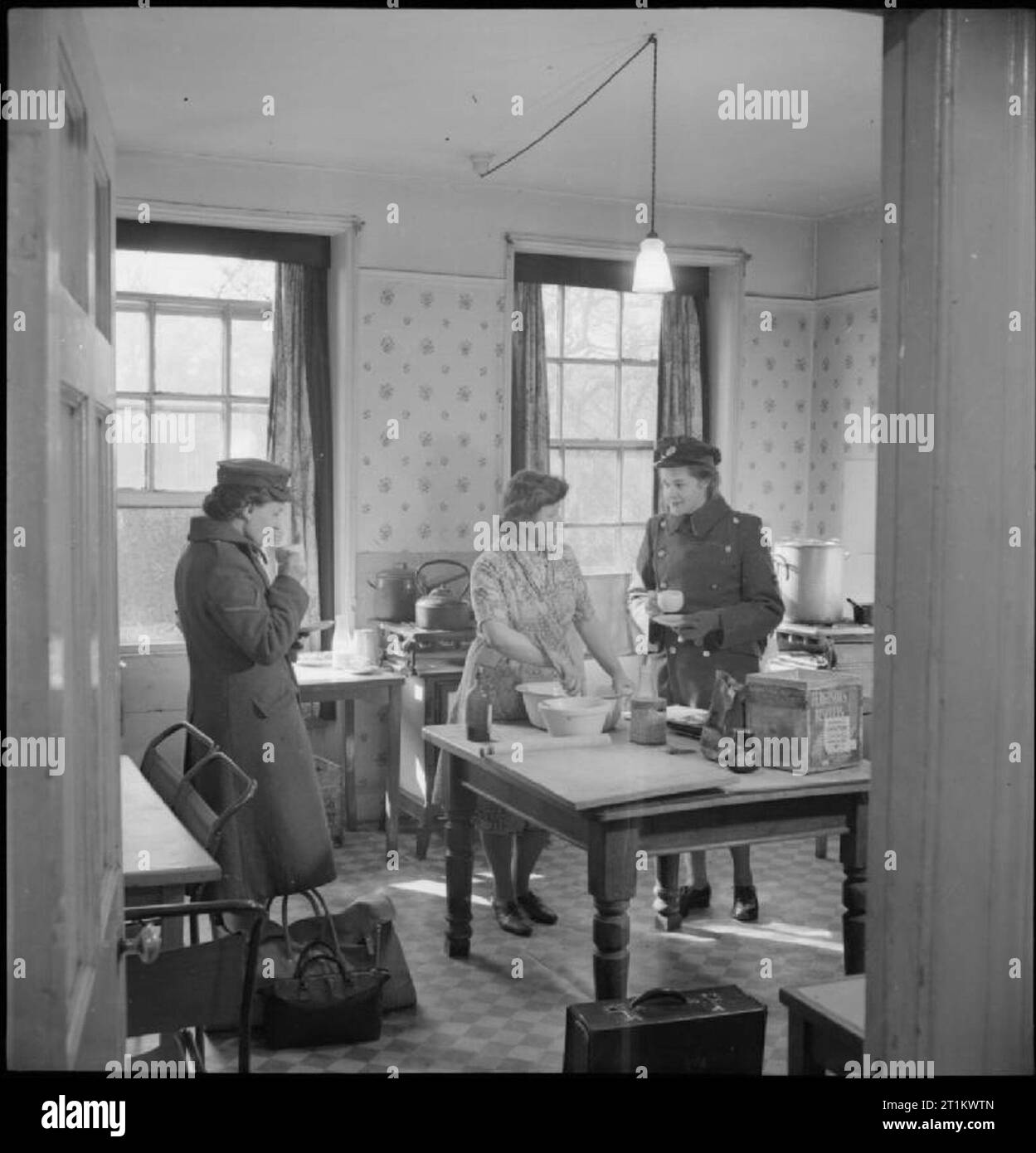 YWCA Clubs- le travail de la Young Women's Christian Association en temps de guerre, Norfolk, Angleterre, Royaume-Uni, 1944 lance Caporal A E Cheeseman (à gauche) de Dunstable, et Mme M G Salter, une WAAF canadienne de Sackville, au Nouveau-Brunswick, profite d’une tasse de thé et d’une conversation avec le cuisinier dans la cuisine avant de quitter le club YWCA au Close à Norwich. Toutes les femmes qui doivent quitter le club avant l'heure du petit déjeuner peuvent aller à la cuisine pour avoir quelque chose à manger avant de partir. Banque D'Images