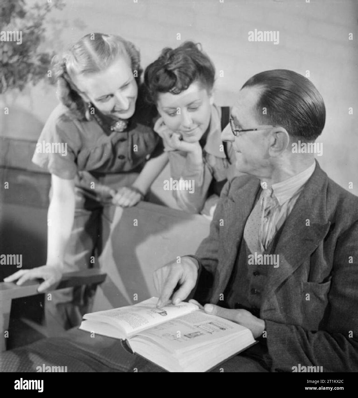 Ballet va à l'usine, de la danse et des animations organisées par le Conseil pour l'encouragement de la musique et des arts, de l'Angleterre, 1943 Danseurs Marguerite Stewart (à gauche) et Olivia Sarel du Ballet Rambert écouter comme Arthur Leach, un stamper's assistant à cette usine, explique son travail à eux avec l'aide d'un livre sur l'ingénierie. Selon la légende originale, Arthur avait déjà été un conducteur de bus. Banque D'Images