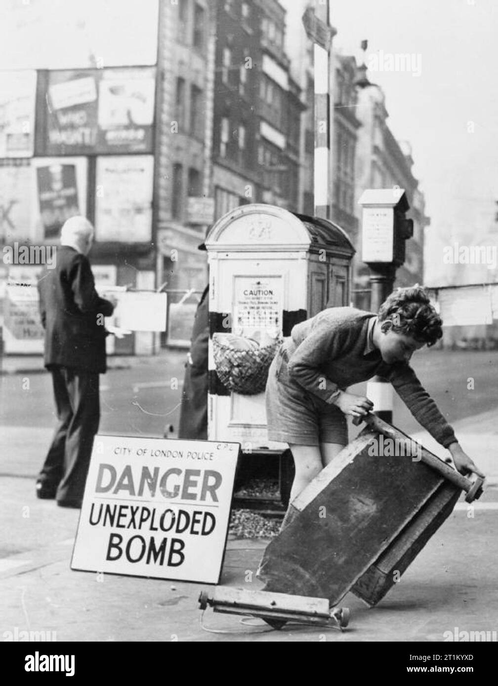 Accueil de la Grande-Bretagne - 1939 avant 1945 un enfant Londres réparait sa voiture jouet dans la rue complètement insensible à la bombe non explosée 'inscription' derrière lui. Banque D'Images