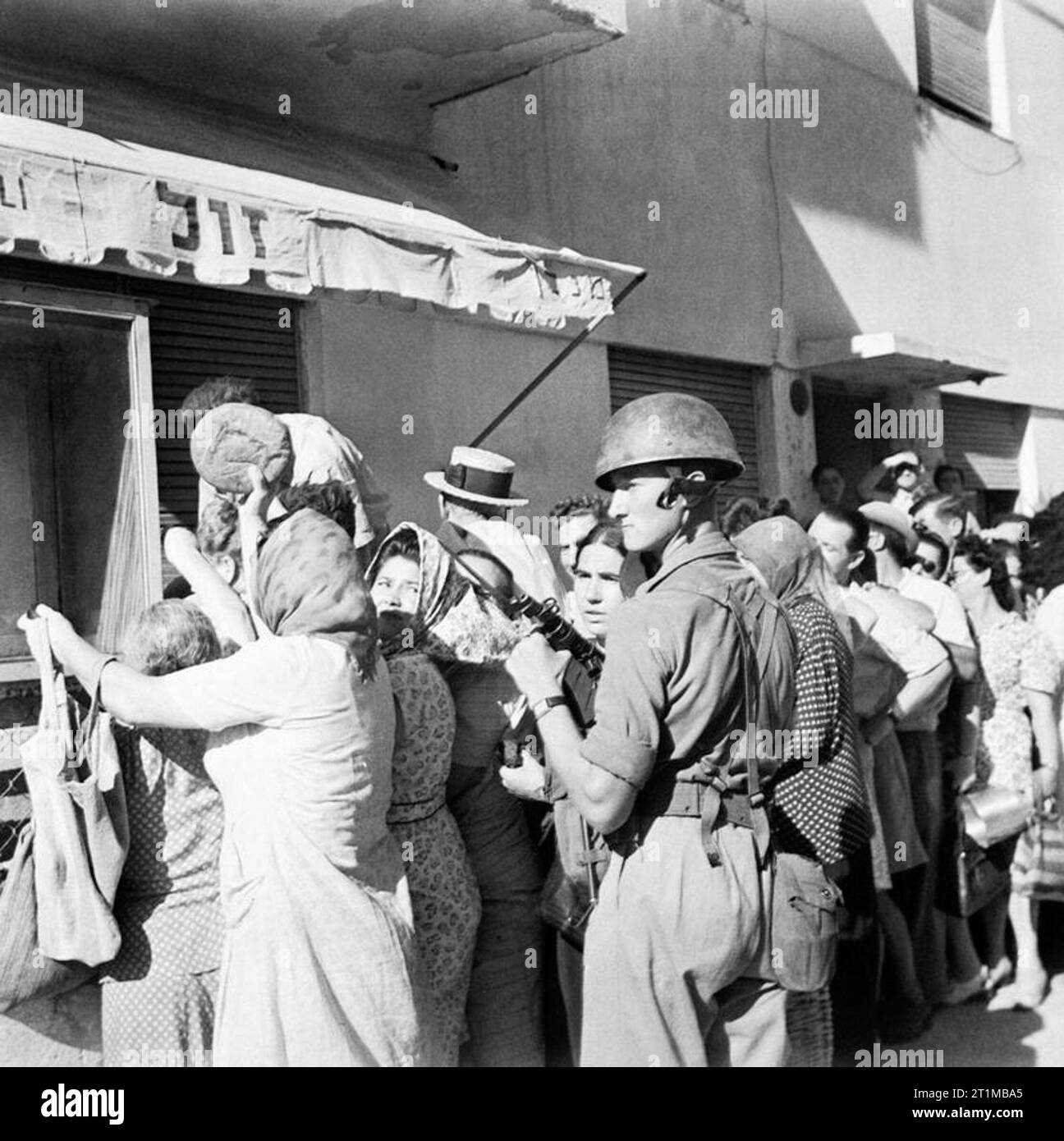 Les forces britanniques au Moyen-Orient, 1945-1947 Après la levée du couvre-feu à Tel Aviv de grandes foules se sont réunis à l'extérieur des commerces alimentaires. Ici un soldat de la 6e Division aéroportée se distingue par le maintien de l'ordre à l'extérieur d'un atelier de boulangerie. Banque D'Images