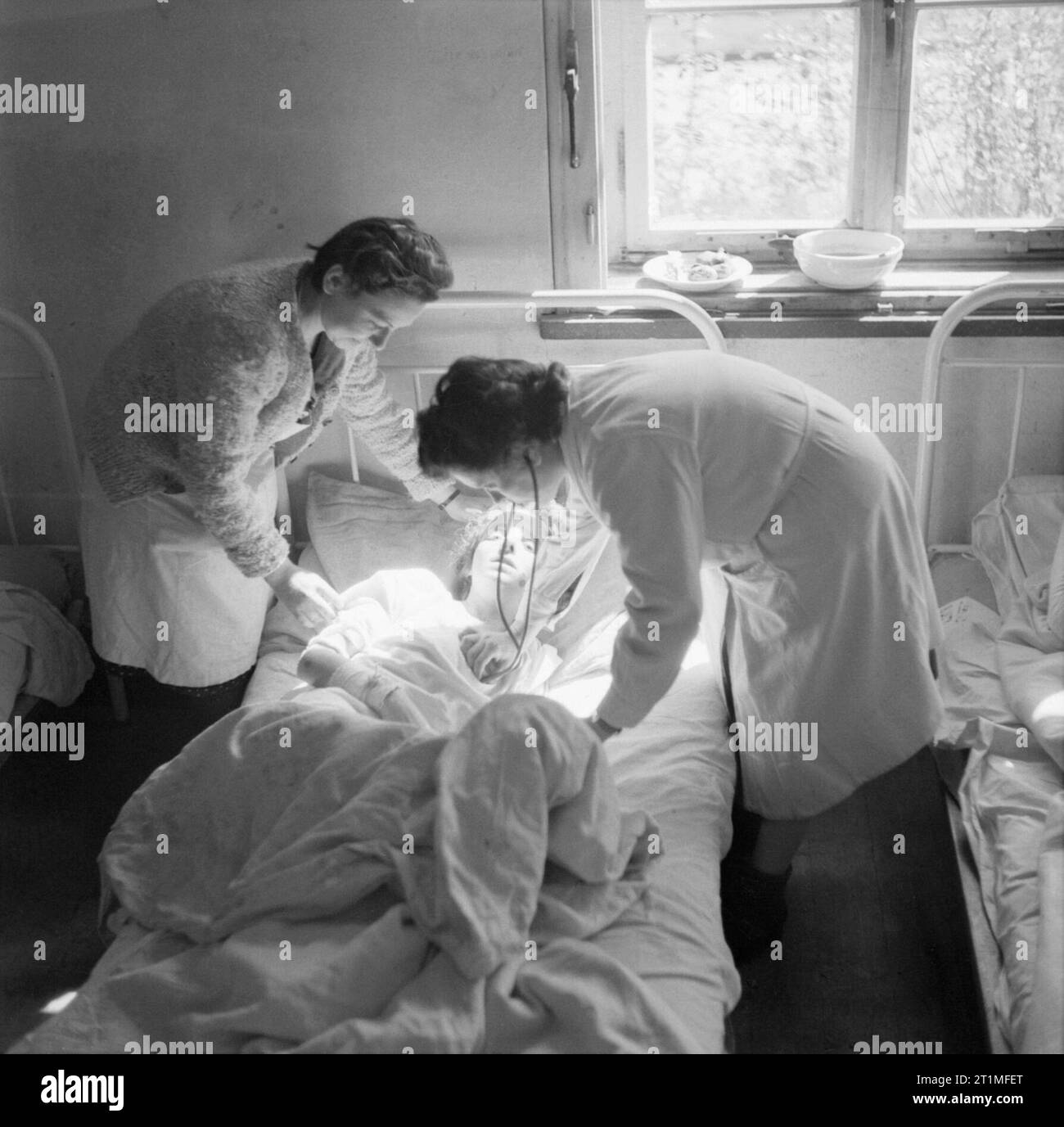 La libération du camp de concentration de Belsen Bergen-avril 1945, un ex-détenu malade du Camp n°1 est pris en charge par le Dr Nysenhauz (à droite), une femme médecin polonais et ancien détenu du camp qui a elle-même venait de se remettre du typhus, au Camp n° 2, Hohne casernes militaires. Elle est assistée de Sœur Renée Erman, une infirmière française qui était aussi un ancien détenu du camp. Les trois femmes dans la photo sont juifs. Banque D'Images