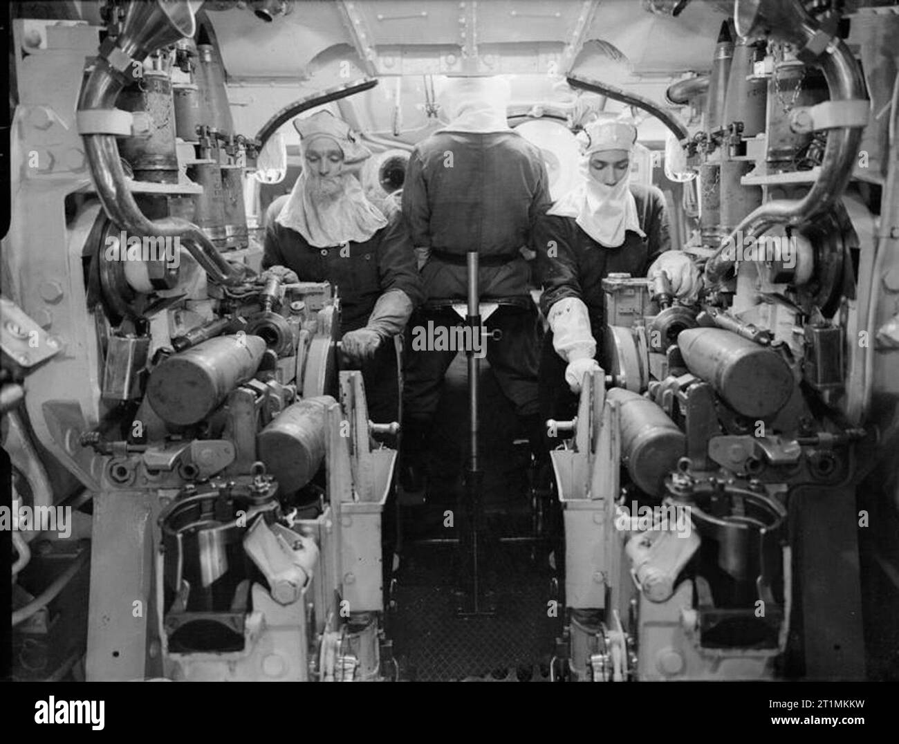 La Royal Navy pendant la Seconde Guerre mondiale, l'intérieur de la d'un jumeau gunhouse 5,25 pouce de Canon Mark II à bord du HMS KING GEORGE V, cet angle est à la recherche le long de la canons. Remarque l'équipage vêtu de flash anti. Les deux membres de l'équipe face à l'exploitation sont le photographe d'un grand angle du levier de levage, qui exploite le shell pour palan automatique lorsque le canon est dans un rôle. Le membre d'équipage avec son dos le photographe semble être à la recherche à travers le regard fenêtre port. Banque D'Images