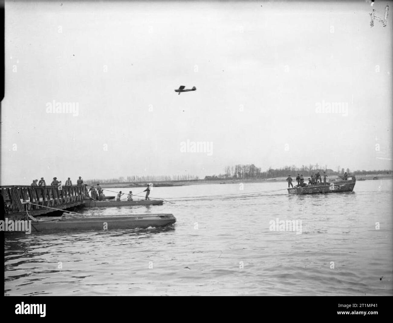 La Royal Navy pendant la Seconde Guerre mondiale, un bateau de débarquement en aidant à la mise en place d'une section du pont après le remorquage de la banque. Un Taylorcraft Auster spotter appareil vole bas dans le milieu de la distance. Cette olcab "Royal Navy"- mobile landing craft de base avancée à Reichswald, l'Allemagne joue un rôle important dans l'armée de passage du Rhin. Banque D'Images