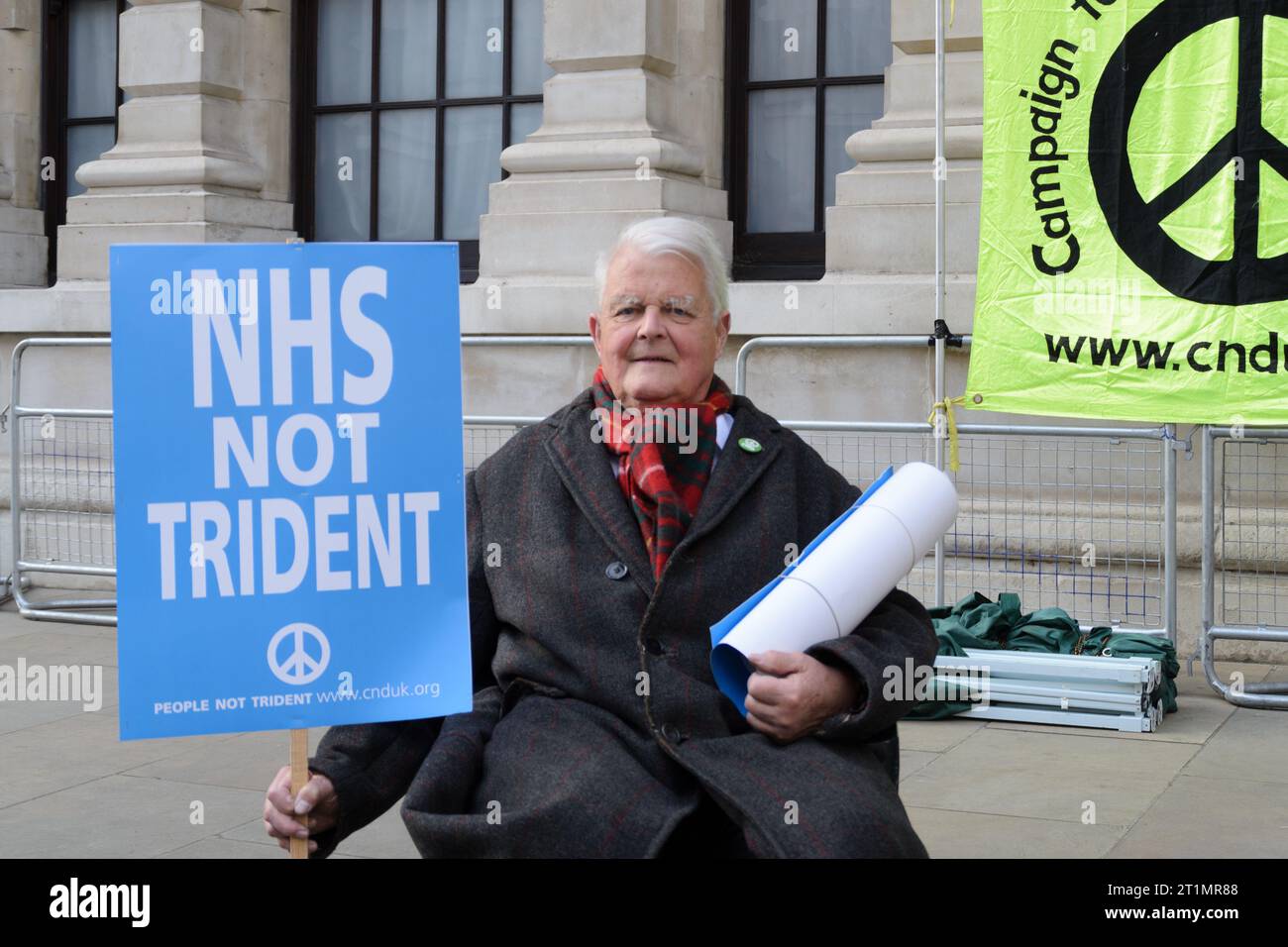 Horse Guards Avenue, Londres, Royaume-Uni - 13 avril 2015 : activiste Bruce Kent et vice-président honoraire du CND assis tenant une pancarte anti Trident. Banque D'Images