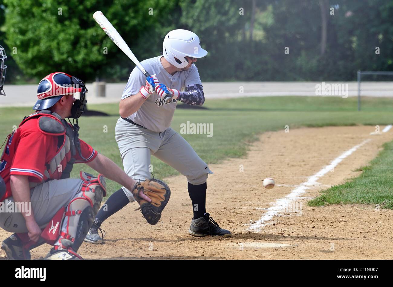 Spring Grove, Illinois, États-Unis. Un batteur prenant un terrain en dessous de la zone de frappe pour une balle lors d'un match de baseball amateur masculin dans la banlieue de Chicago. Banque D'Images