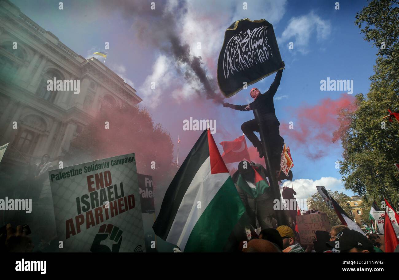 Londres, Royaume-Uni. 14 octobre 2023. Un manifestant s'accroche à un feu tricolore tout en tenant un drapeau avec une écriture arabe et une éruption noire à Whitehall. Des groupes se sont réunis pour marcher jusqu'à Downing Street pour soutenir le peuple palestinien avant les représailles israéliennes après la récente attaque du Hamas contre des civils israéliens. Pour tenter de dissiper les tensions, le Ministre de l ' intérieur a rappelé aux policiers qu ' agiter des drapeaux palestiniens et utiliser des chants et des slogans pourrait contrevenir à la loi sur l ' ordre public. Crédit : SOPA Images Limited/Alamy Live News Banque D'Images