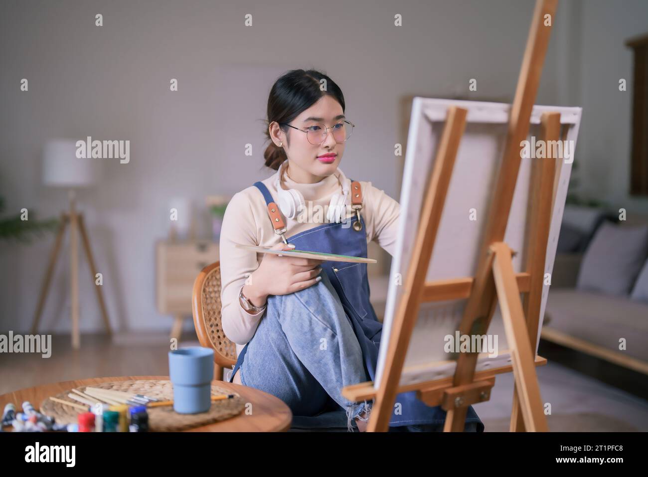 Jeune artiste féminine asiatique porter un casque dans son cou et utiliser des œuvres d'art de peinture au pinceau sur toile. Banque D'Images