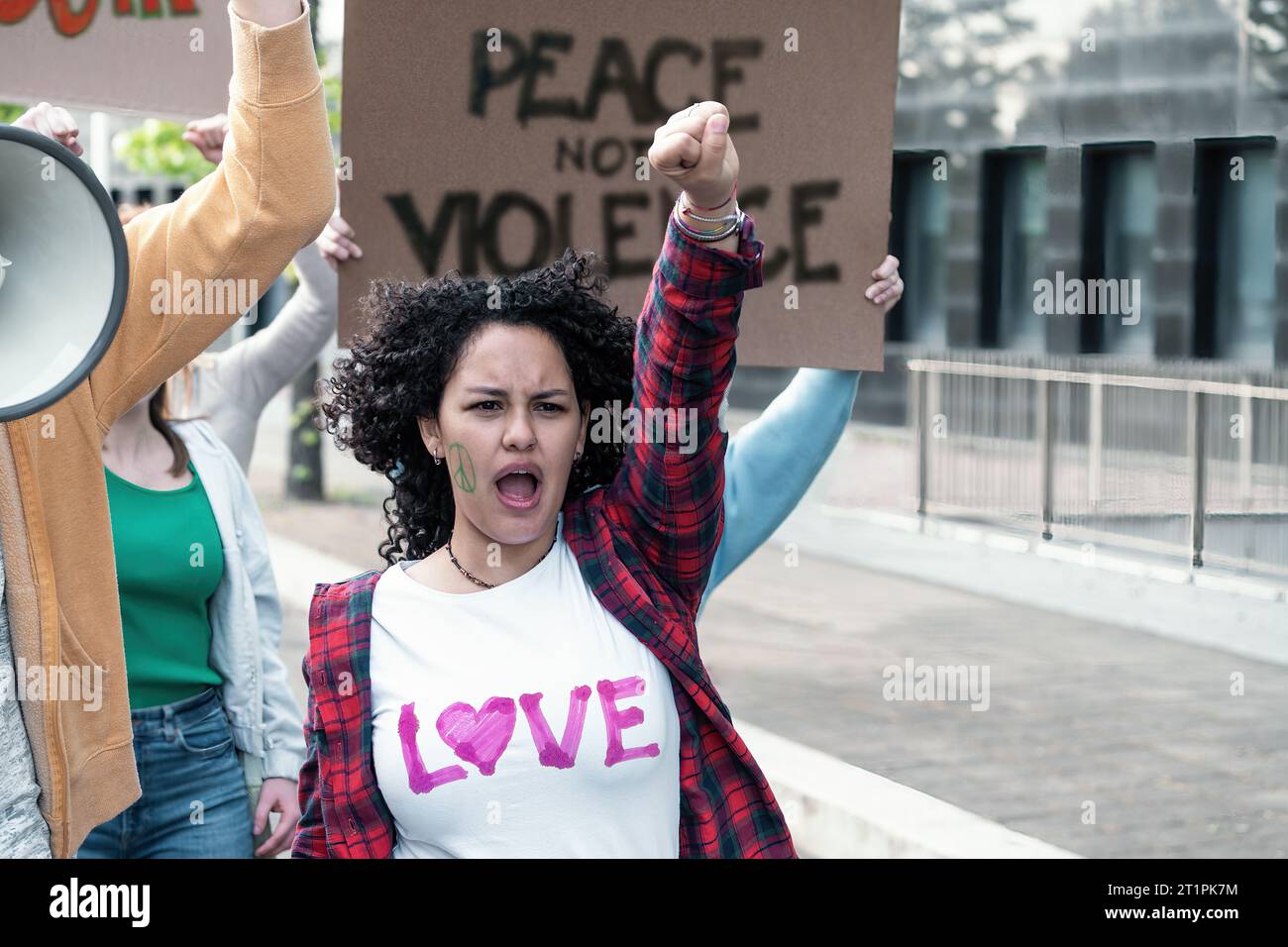 Une jeune femme fervente aux cheveux bouclés lève le poing dans un geste puissant, symbolisant la défiance et la demande de changement. Derrière elle, une autre prote Banque D'Images