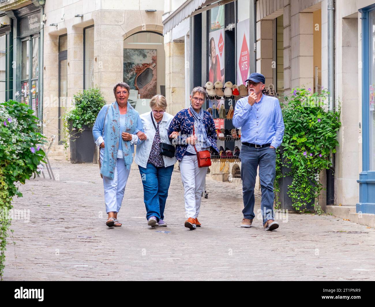 Homme plus âgé habillé avec désinvolture et trois femmes marchant le long de la rue tranquille de la ville - Loches, Indre-et-Loire (37), France. Banque D'Images