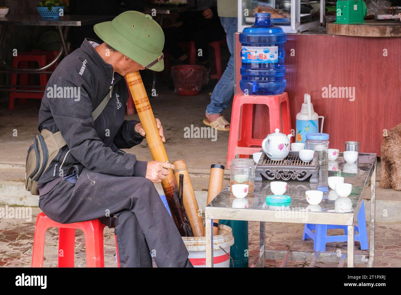 Bac Ha, Vietnam. Homme fumant une pipe en bambou au stand de rafraîchissement du trottoir. Province de Lao Cai. Banque D'Images