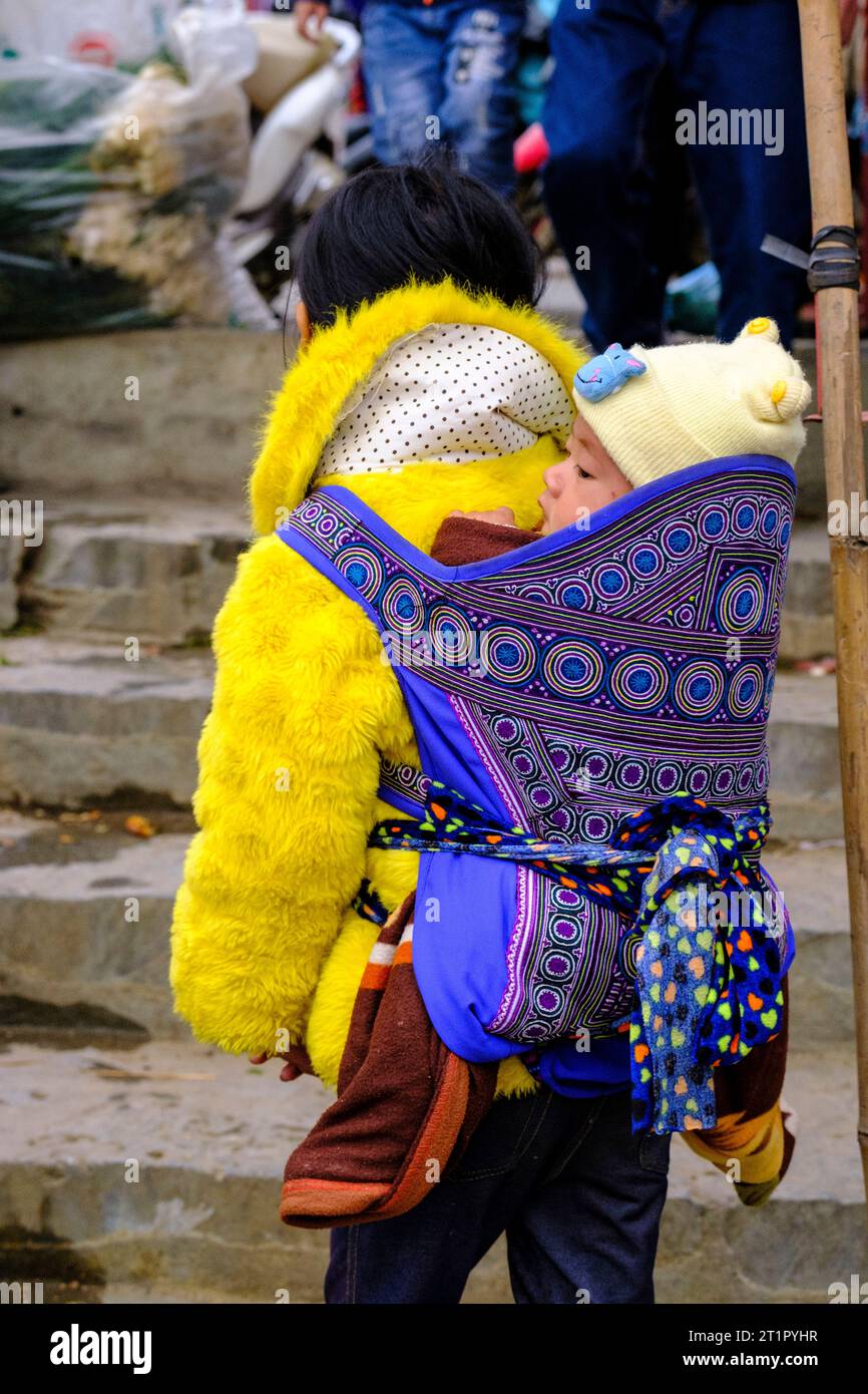 Bac Ha, Vietnam. Scène du marché du dimanche. Jeune fille Hmong portant un bébé sur son dos. Province de Lao Cai. Banque D'Images