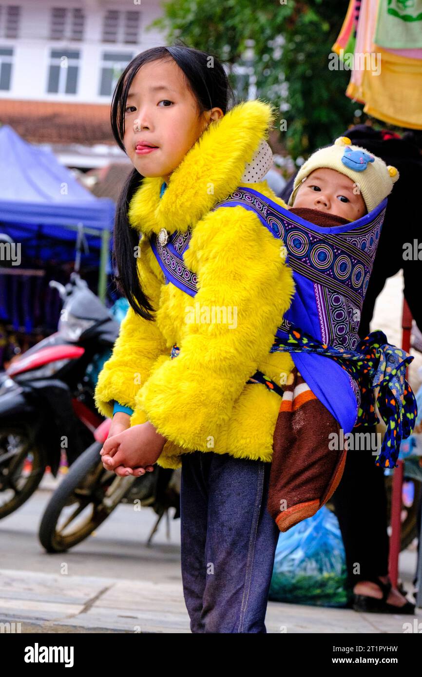 Bac Ha, Vietnam. Scène du marché du dimanche. Jeune fille Hmong portant un bébé sur son dos. Province de Lao Cai. Banque D'Images