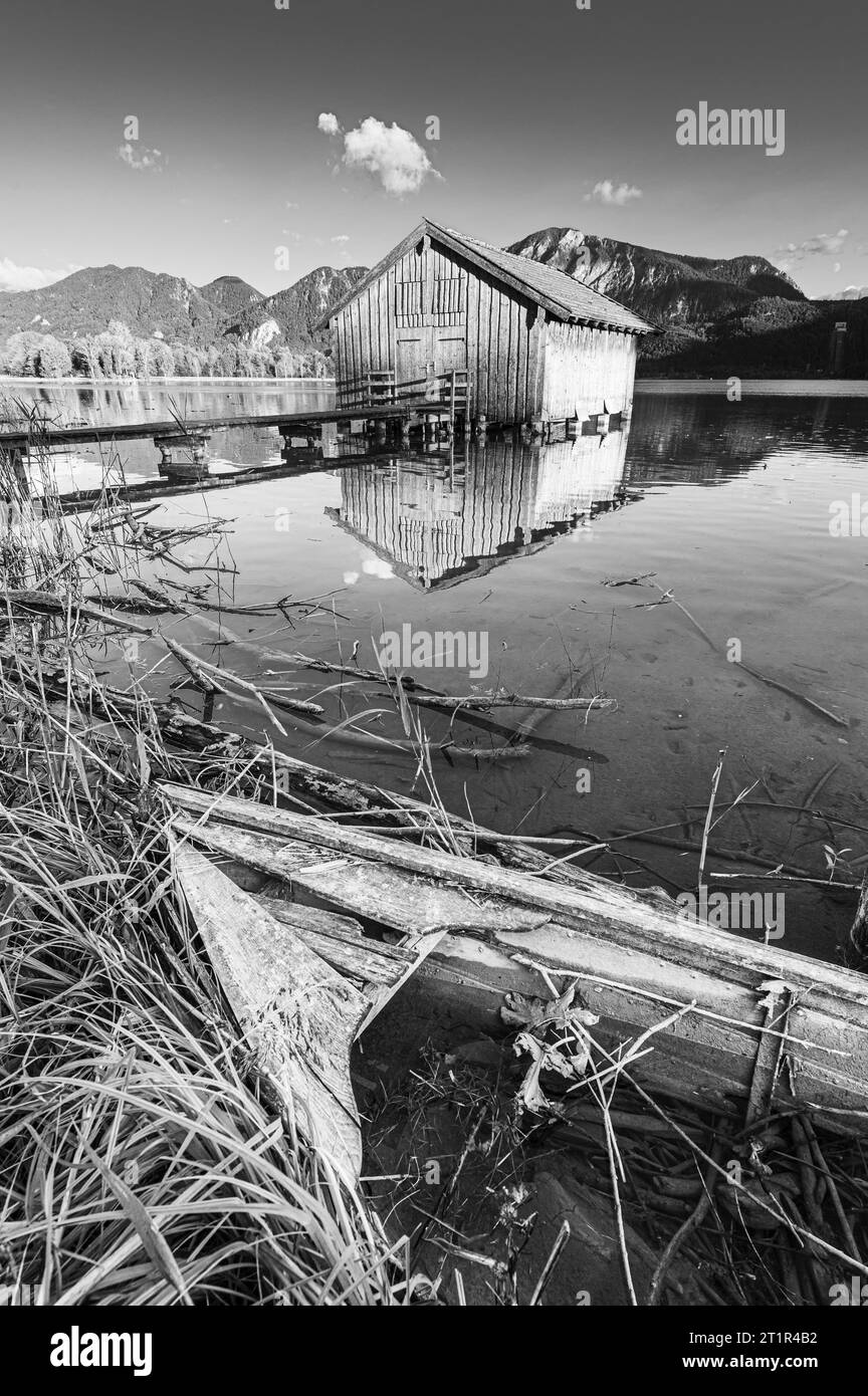 Bateau en bois pourri devant un hangar à bateaux sur la rive du Kochelsee devant le Herzogstand et Jochberg dans le soleil du soir en automne Banque D'Images