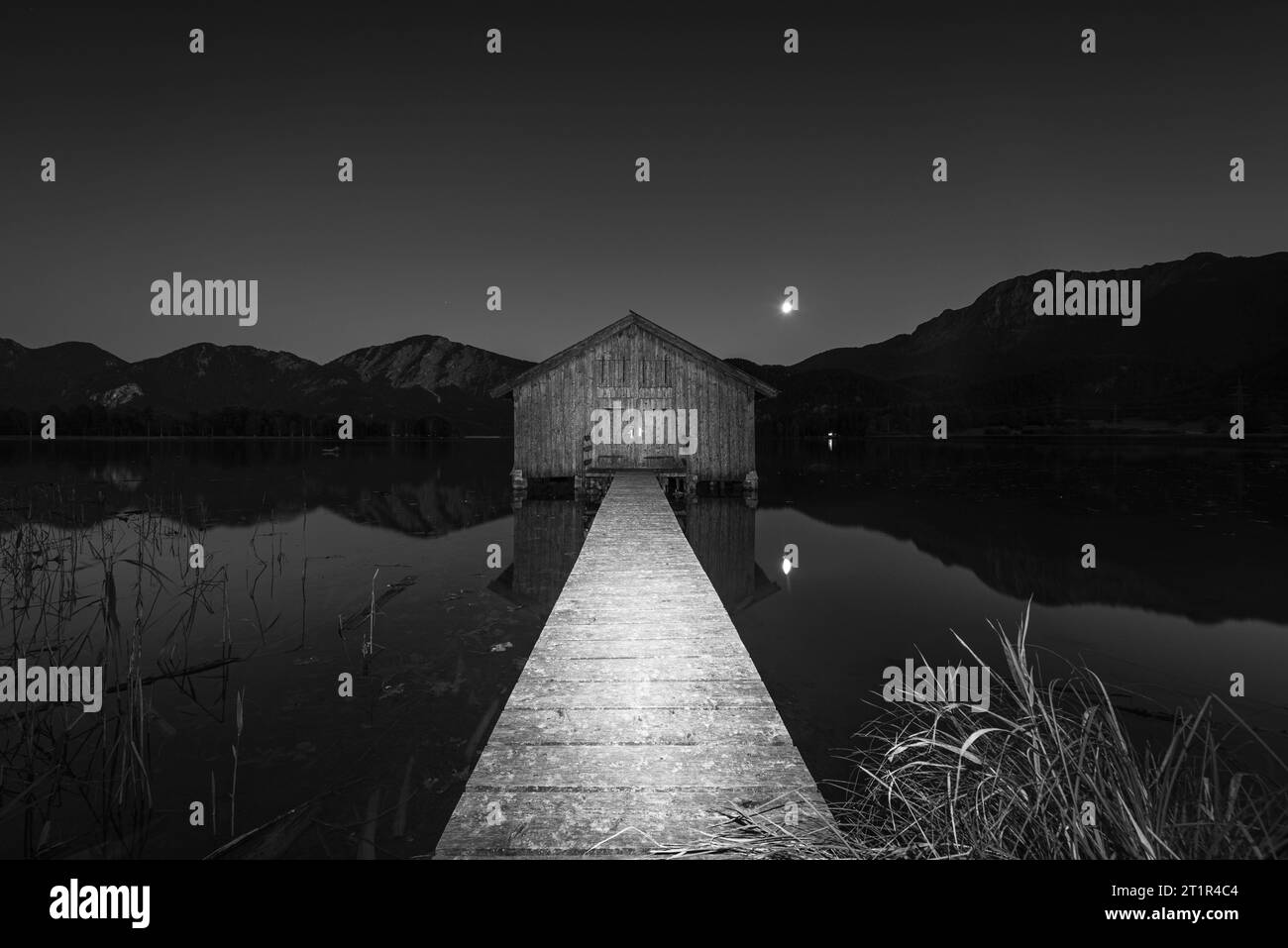 Lever de la lune au-dessus d'un hangar à bateaux en bois sur la rive du lac Kochelsee en face du Herzogstand et du Jochberg au crépuscule en automne, Bavière, Allemagne Banque D'Images