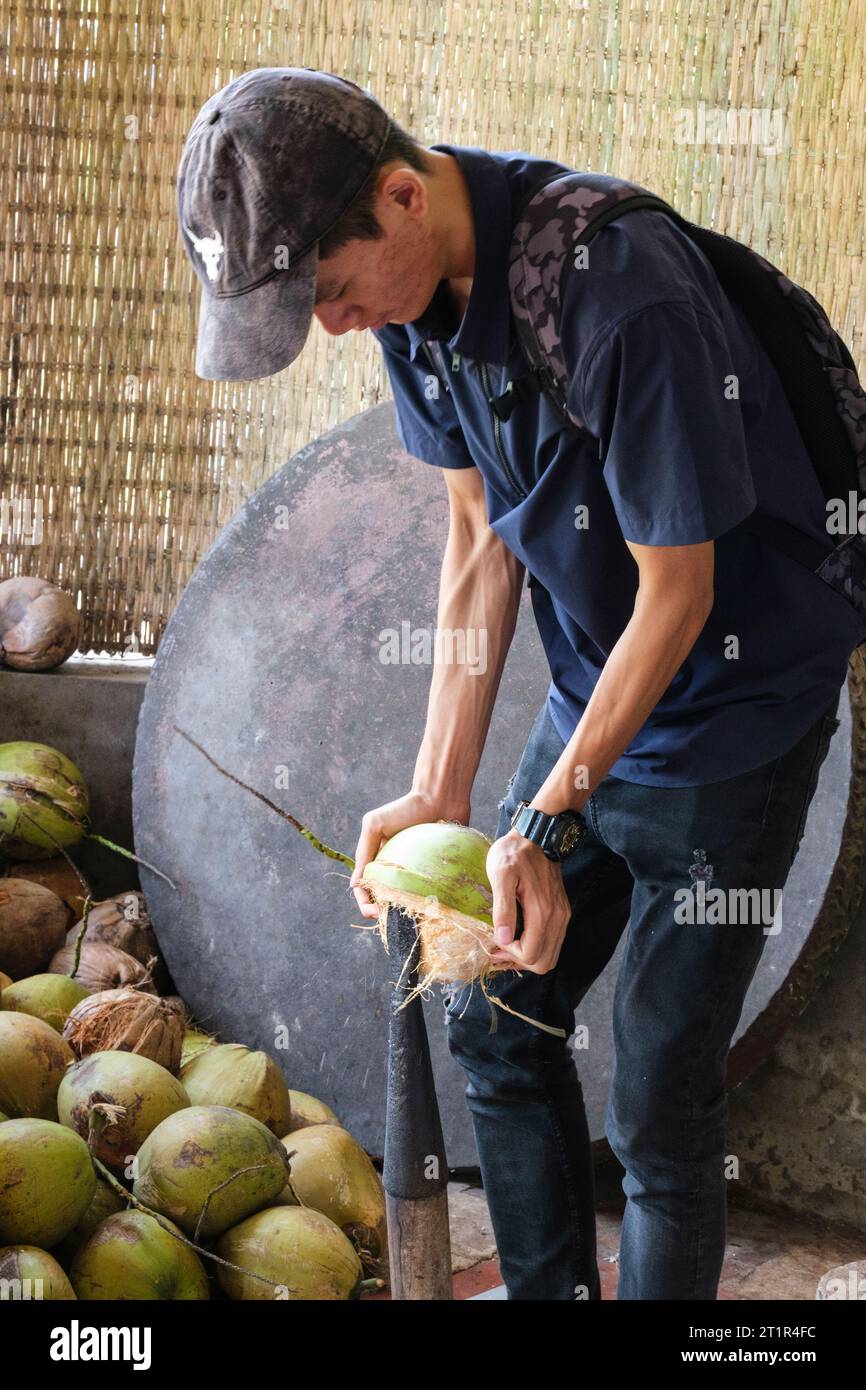 Homme démontrant l'ouverture d'une noix de coco, à une usine de bonbons de noix de coco du fleuve Mékong, Vietnam. Banque D'Images