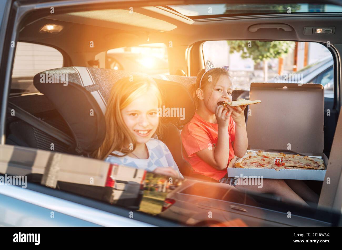 Deux sœurs souriantes et positives sont heureuses de manger une pizza italienne juste cuite dans les sièges d'enfant sur le siège arrière de la voiture. Bonne enfance, restauration rapide ea Banque D'Images