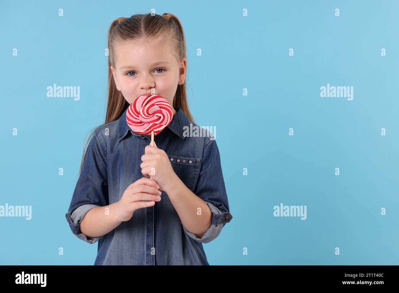 Mignonne petite fille léchant brillant sucette tourbillon sur fond bleu clair, espace pour le texte Banque D'Images