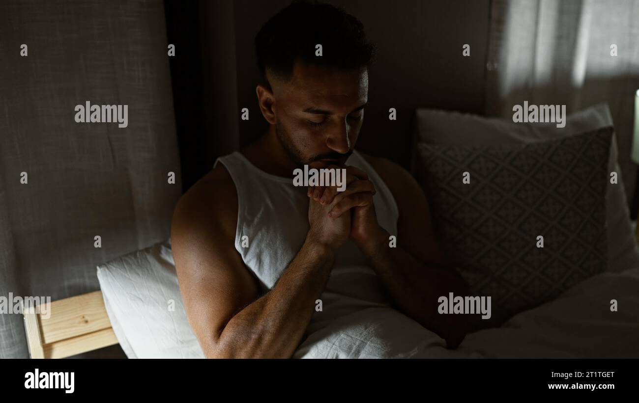 Jeune homme arabe assis sur le lit priant dans la chambre à coucher Banque D'Images