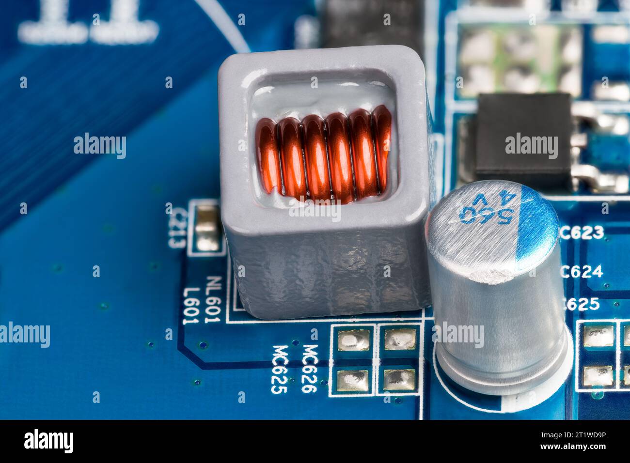 Gros plan de la bobine électronique et du condensateur électrolytique sur le fond de la carte de circuit imprimé bleue. Fil de cuivre de l'inducteur intégré en époxy dans un boîtier gris. Banque D'Images