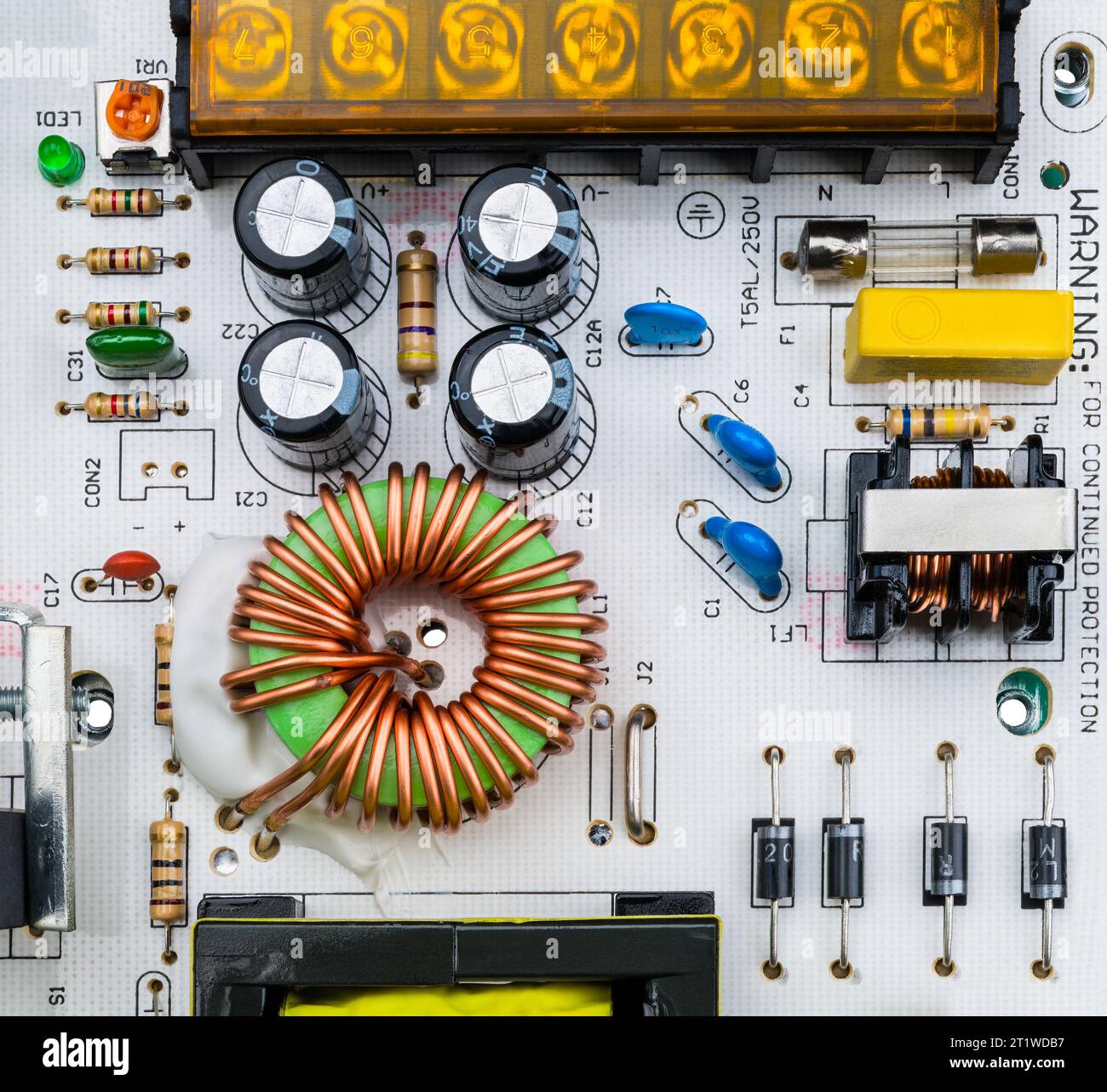 Gros plan de composants électroniques sur une carte de circuit imprimé blanche. Bobine toroïdale et divers condensateurs, fusible électrique et trimmer de résistance ou diodes. Banque D'Images