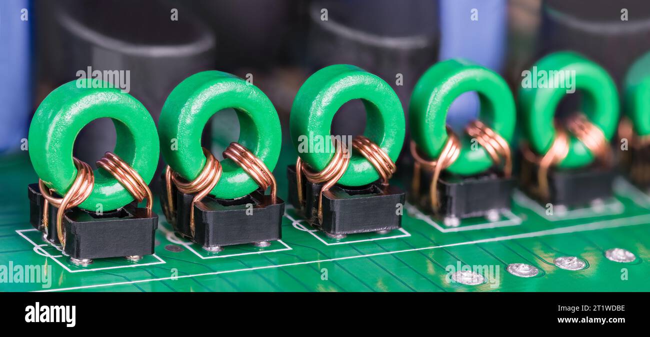 Rangée d'inductances de transformateur toroïdal sur ci. Gros plan de bobines électroniques avec fil de cuivre sur noyau de ferrite vert dans des supports noirs. Plaque de circuit imprimé. Banque D'Images